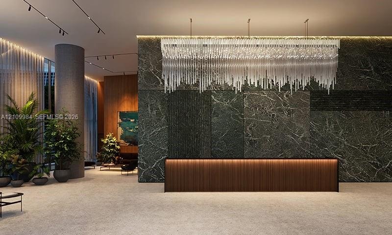 Lobby featuring a stone-clad accent wall, linear crystal chandelier, integrated under-cabinet lighting, wood-panel reception desk, and recessed track 