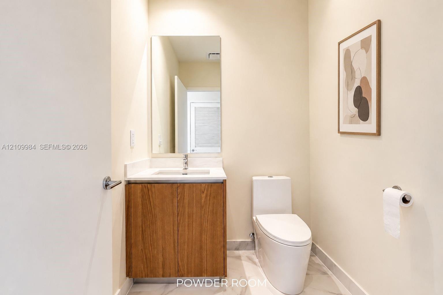 Wood-finish vanity cabinet, white solid-surface countertop with integrated basin, floor-to-ceiling mirror, and stone-finish tile flooring