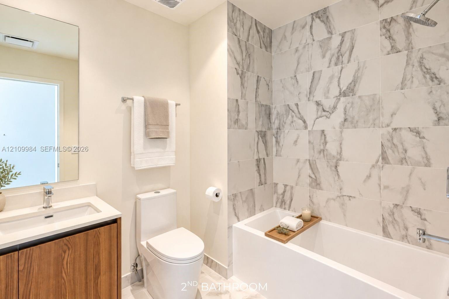 Bathroom featuring a wood-finish vanity with a quartz countertop, rectangular basin, large wall-mounted mirror, and a soaking tub with full-height sto