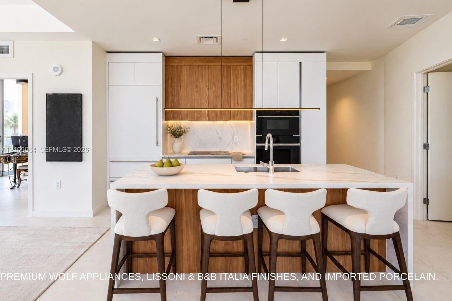 Kitchen featuring an expansive center island with a stone-finish countertop, integrated built-in appliances, flat-panel cabinetry in white and natural
