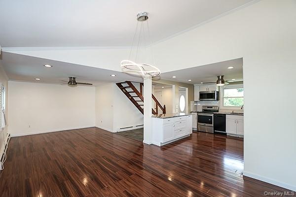 Unfurnished living room featuring ceiling fan, a chandelier, dark wood finished floors, stairway, and vaulted ceiling
