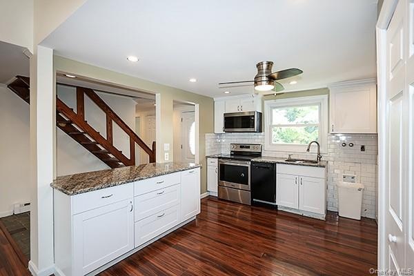 Kitchen featuring white cabinetry, stainless steel appliances, dark stone counters, dark wood-style flooring, and decorative backsplash