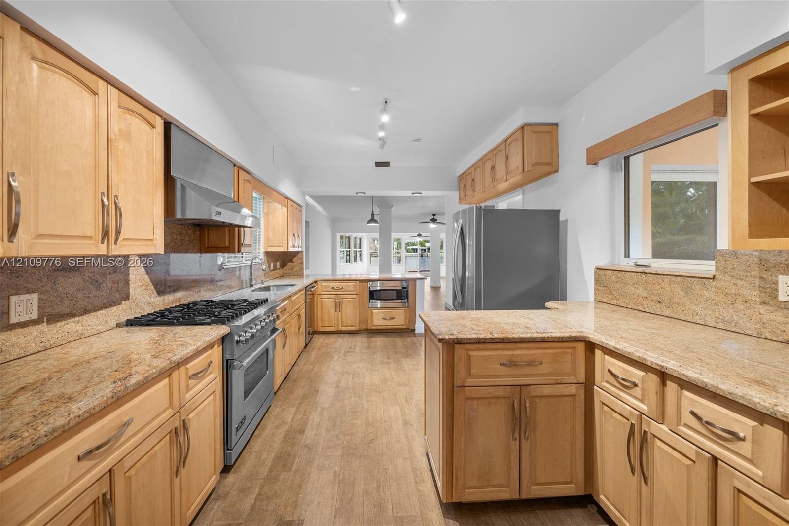 Kitchen featuring light-finish cabinetry, stone countertops, stainless steel gas range with a matching range hood, and wood-finish flooring