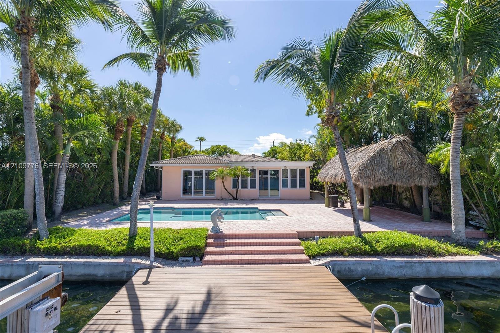 Waterfront property featuring a private dock, swimming pool, paved patio, and thatched-roof tiki structure