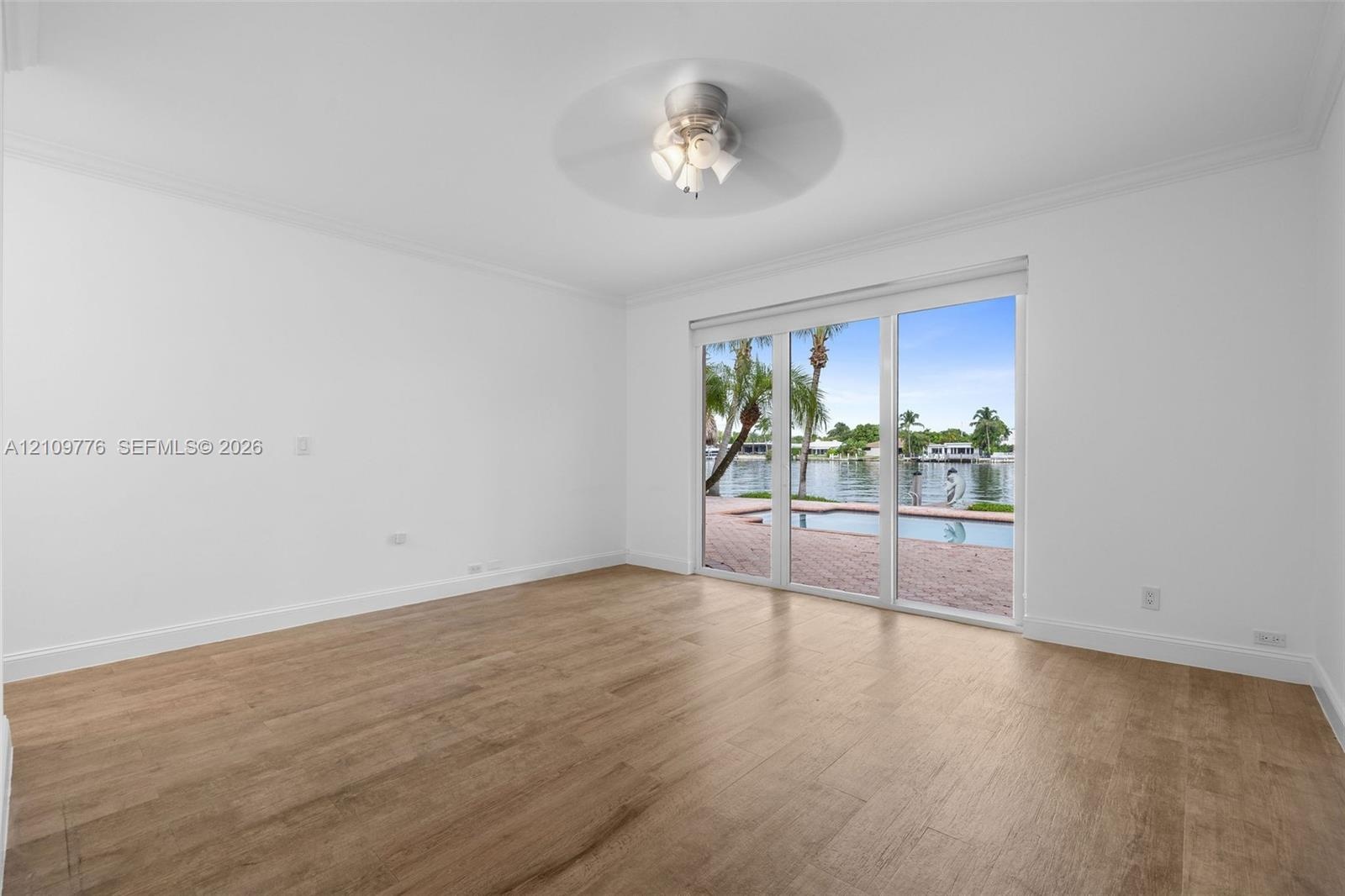 Interior space featuring wood-finish flooring, crown molding, a central ceiling fan with multi-light fixture, and sliding glass doors with access to a