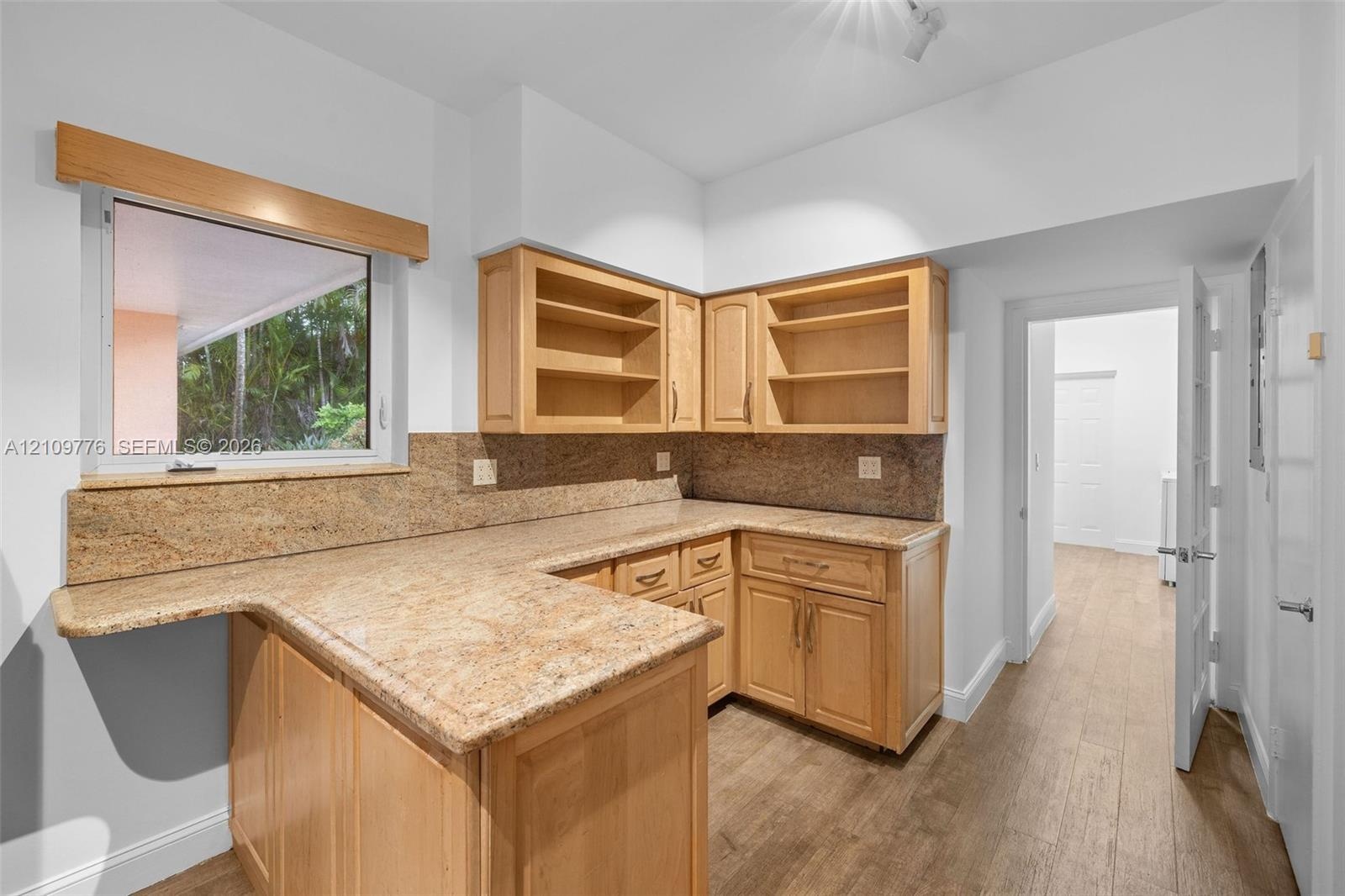 Kitchen featuring natural wood cabinetry, stone countertops, stone backsplash, wood-finish flooring, and a single-pane window with a wood trim accent