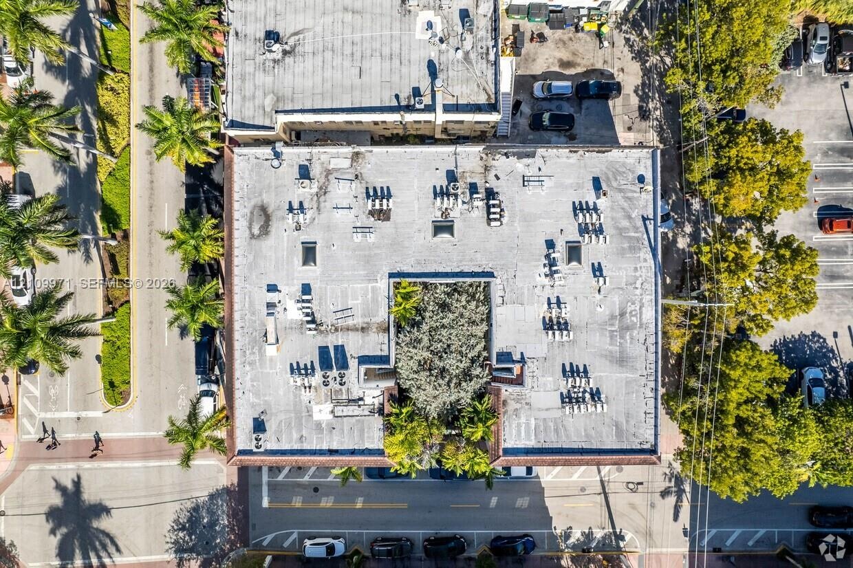 Aerial perspective of a commercial structure featuring a central courtyard with mature landscaping, a flat roof, and paved street-level parking
