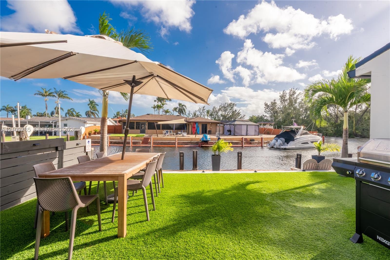 Waterfront patio featuring synthetic turf, wood-tone fencing, and direct canal access with bulkhead docking