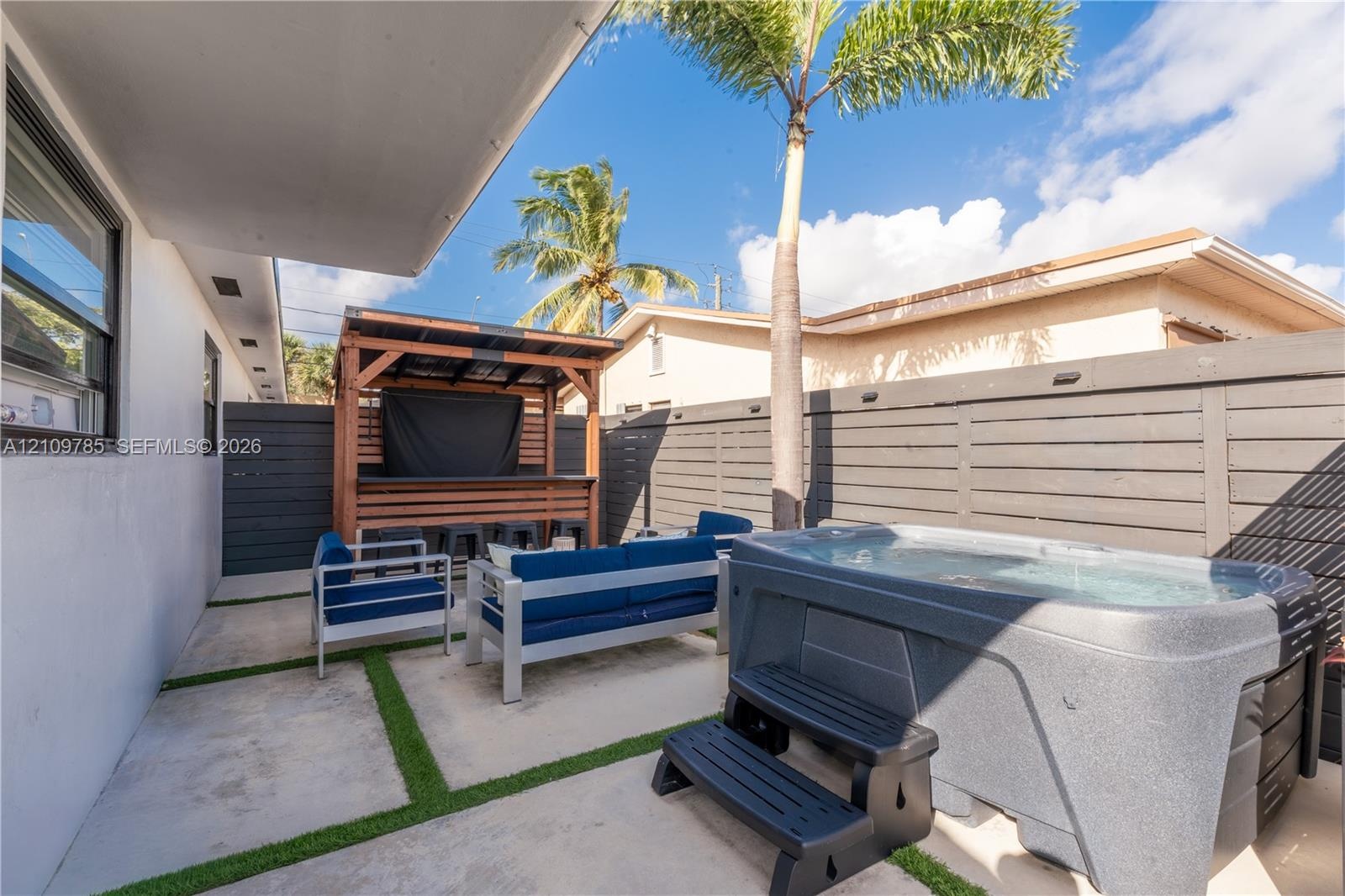Outdoor living area featuring a concrete patio with turf-grid detailing, a built-in bar, a hot tub, privacy fencing