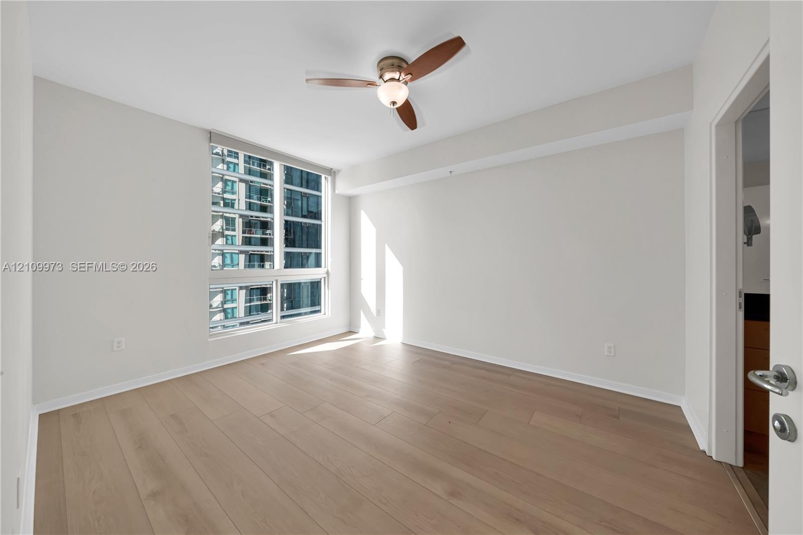 Neutral-toned interior featuring wide-plank wood-finish flooring, floor-to-ceiling windows, and a three-blade ceiling fan with an integrated light fix