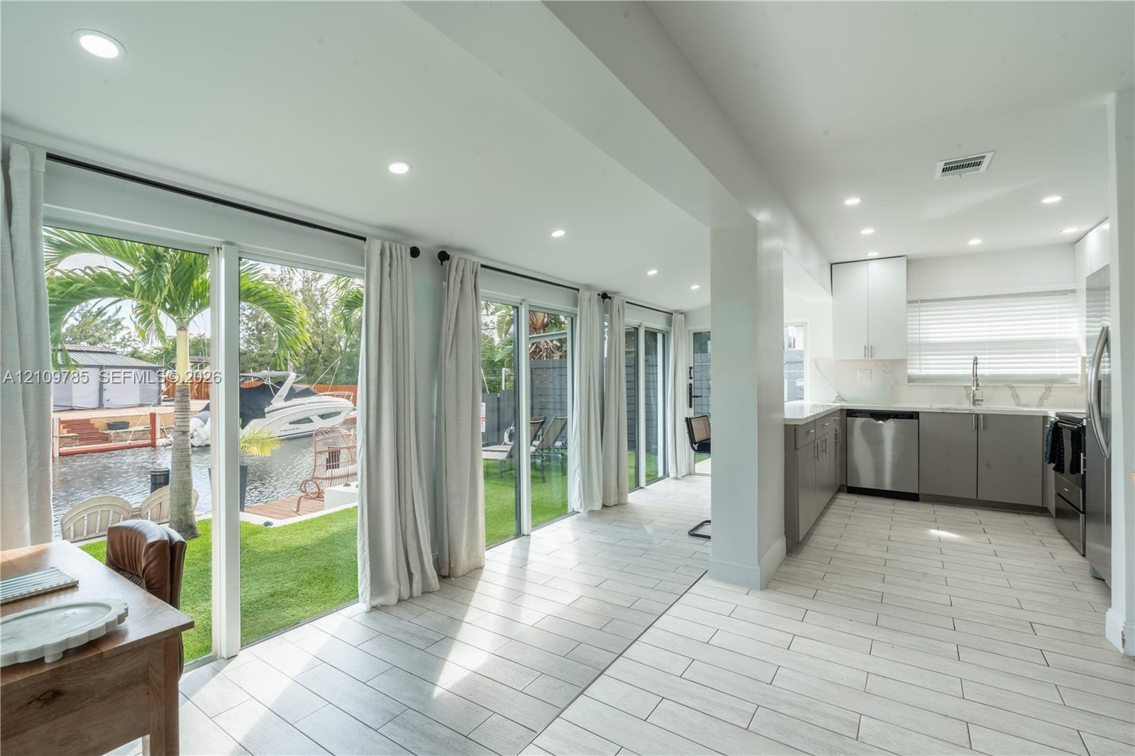 Kitchen featuring stainless steel appliances, white upper cabinetry, grey lower cabinetry, and recessed lighting, paired with floor-to-ceiling glass s
