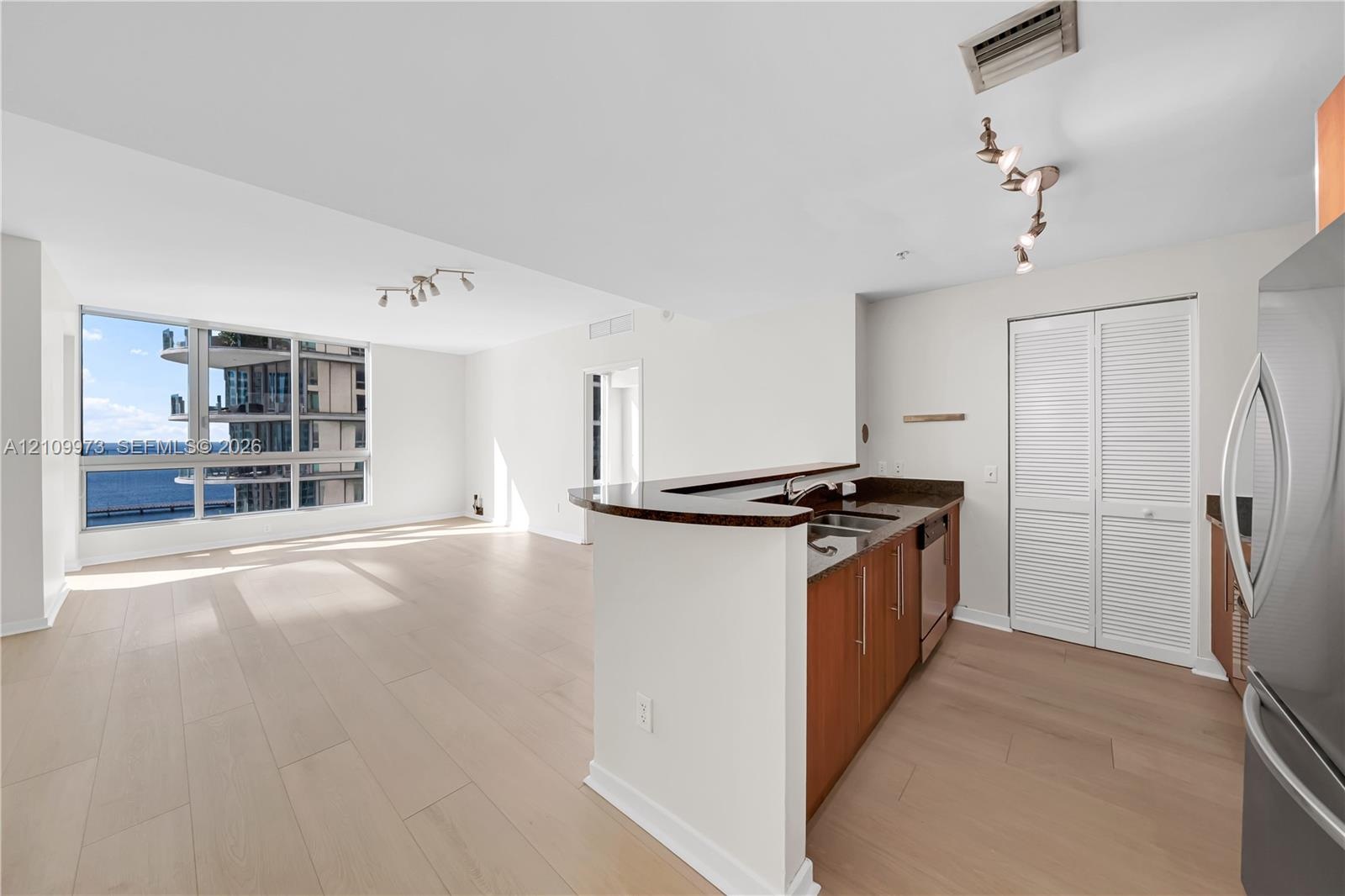 Open-concept living space featuring wood-finish flooring, floor-to-ceiling windows, natural stone kitchen countertops, and track lighting