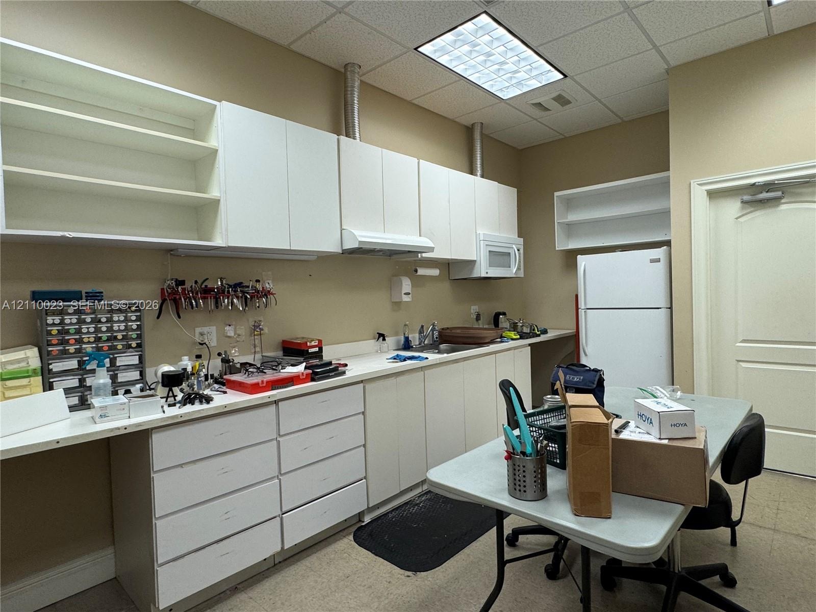 Extensive white cabinetry with upper shelving, solid-surface countertops, built-in sink, and drop-in ceiling lighting