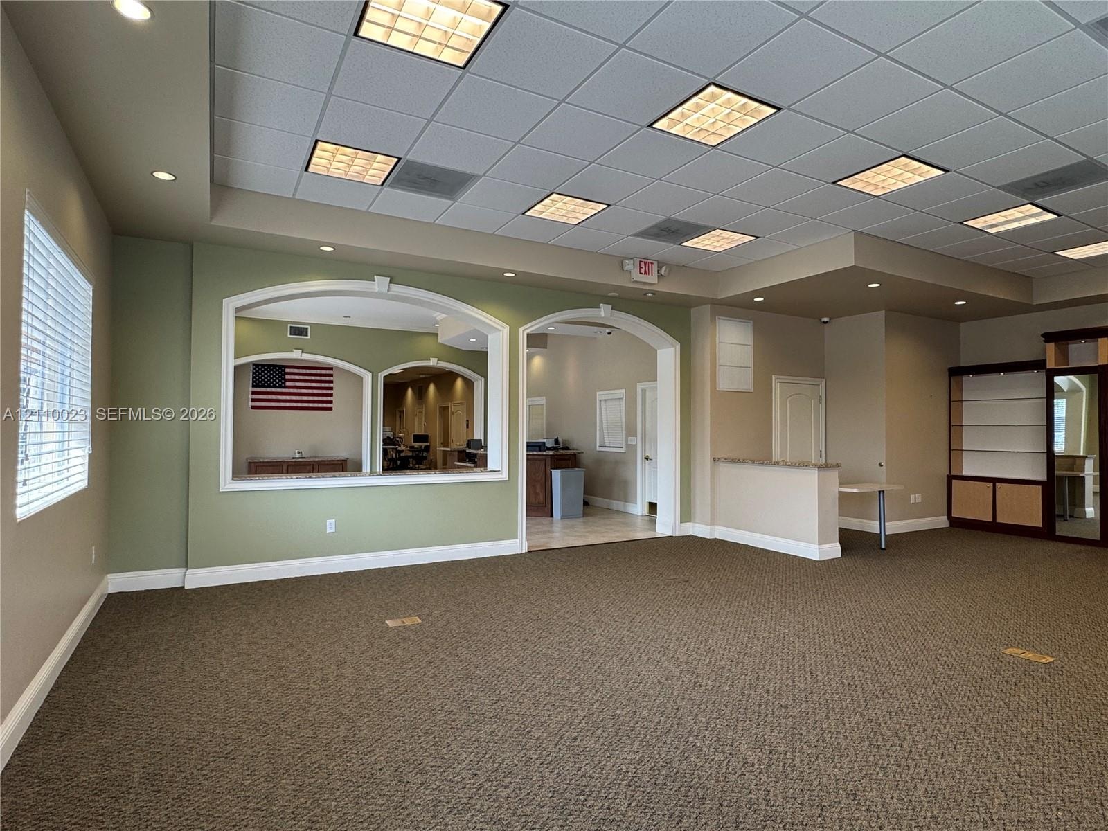 Expansive interior featuring a recessed tray ceiling with integrated drop-tile panels, decorative arched wall cutouts, built-in shelving, and neutral 