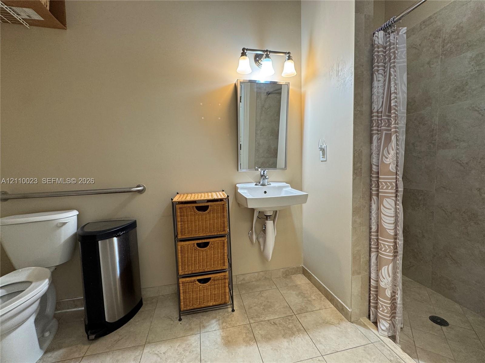 Bathroom featuring a wall-mounted sink with a chrome faucet, medicine cabinet with integrated lighting, tiled walk-in shower, and horizontal grab bar