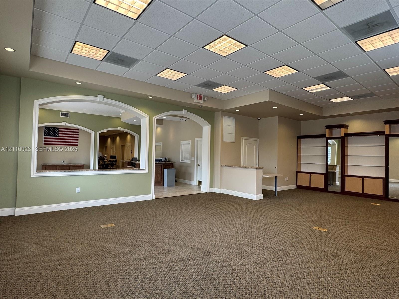 Expansive interior space featuring a drop ceiling with recessed lighting, integrated built-in cabinetry, dual arched wall cutouts, and a neutral color
