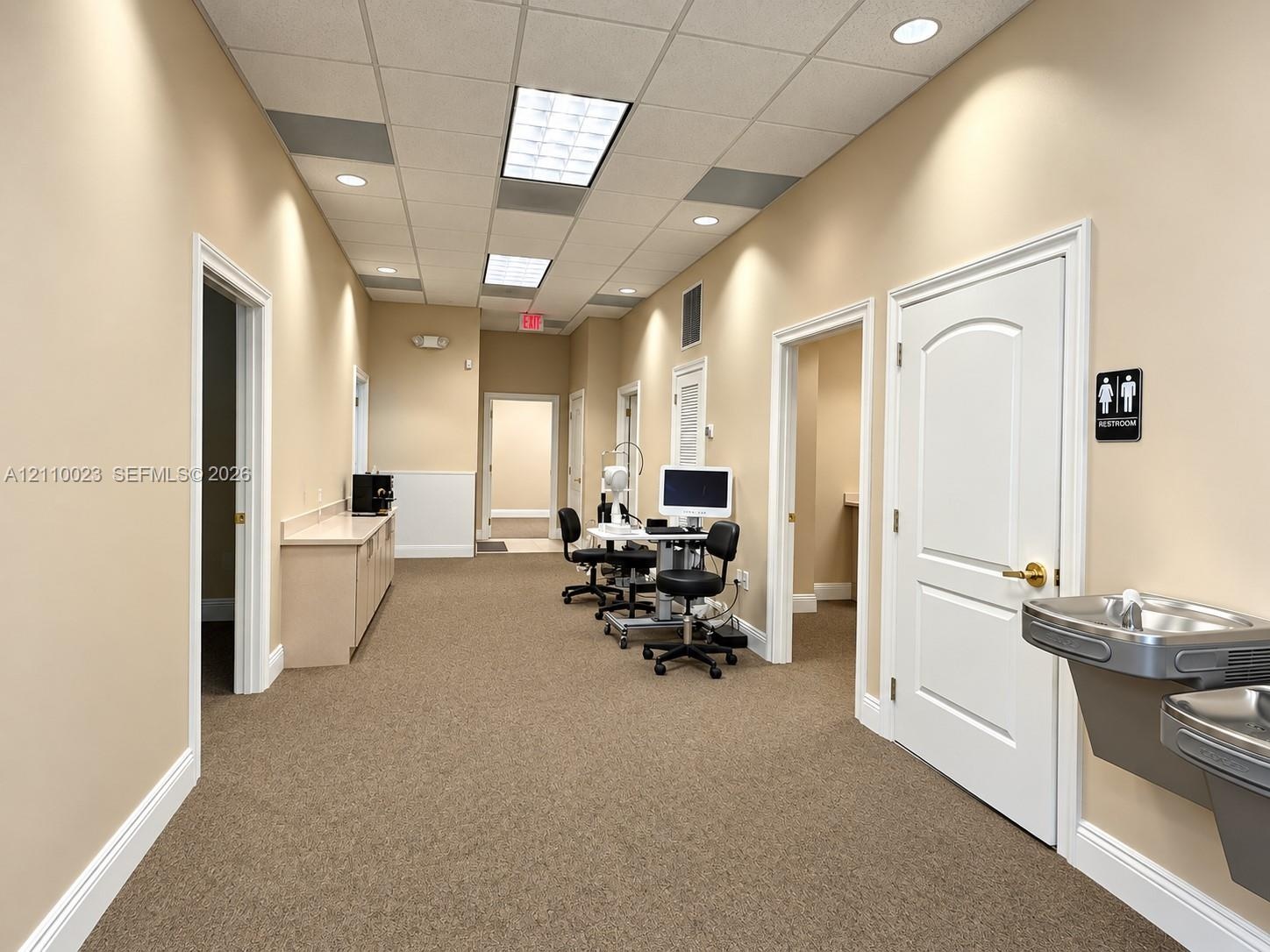 Interior corridor featuring neutral wall finishes, drop ceiling with recessed lighting, carpeted flooring, built-in cabinetry with solid-surface count