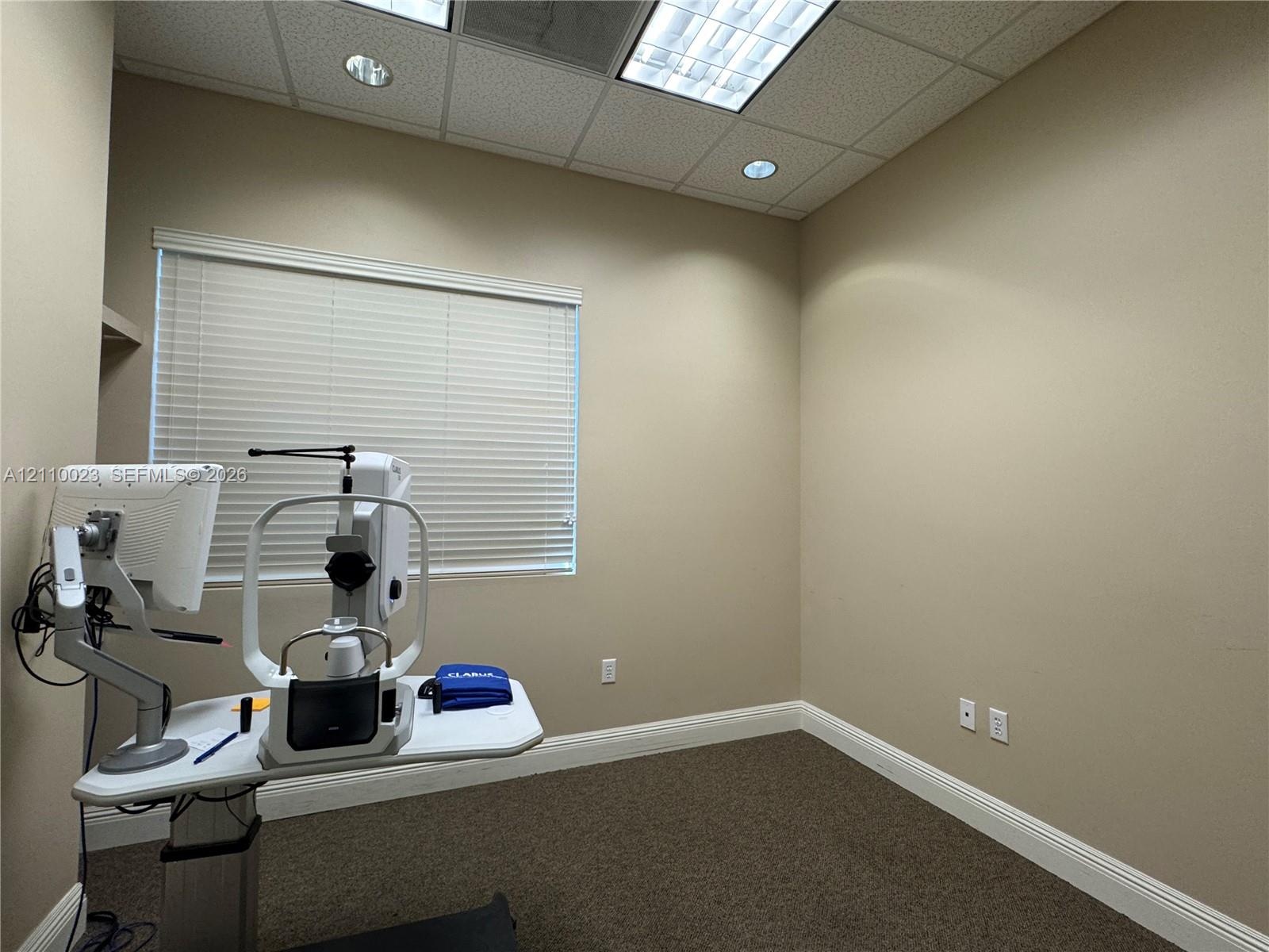 Neutral wall tones, carpeted flooring, horizontal blinds, and a suspended drop ceiling with recessed lighting