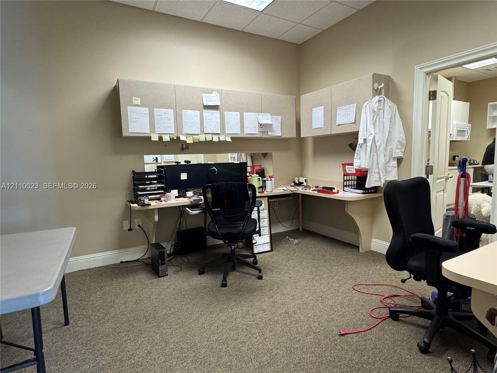 Built-in desk workspace featuring neutral-toned cabinetry, laminate countertops, and acoustic drop ceiling