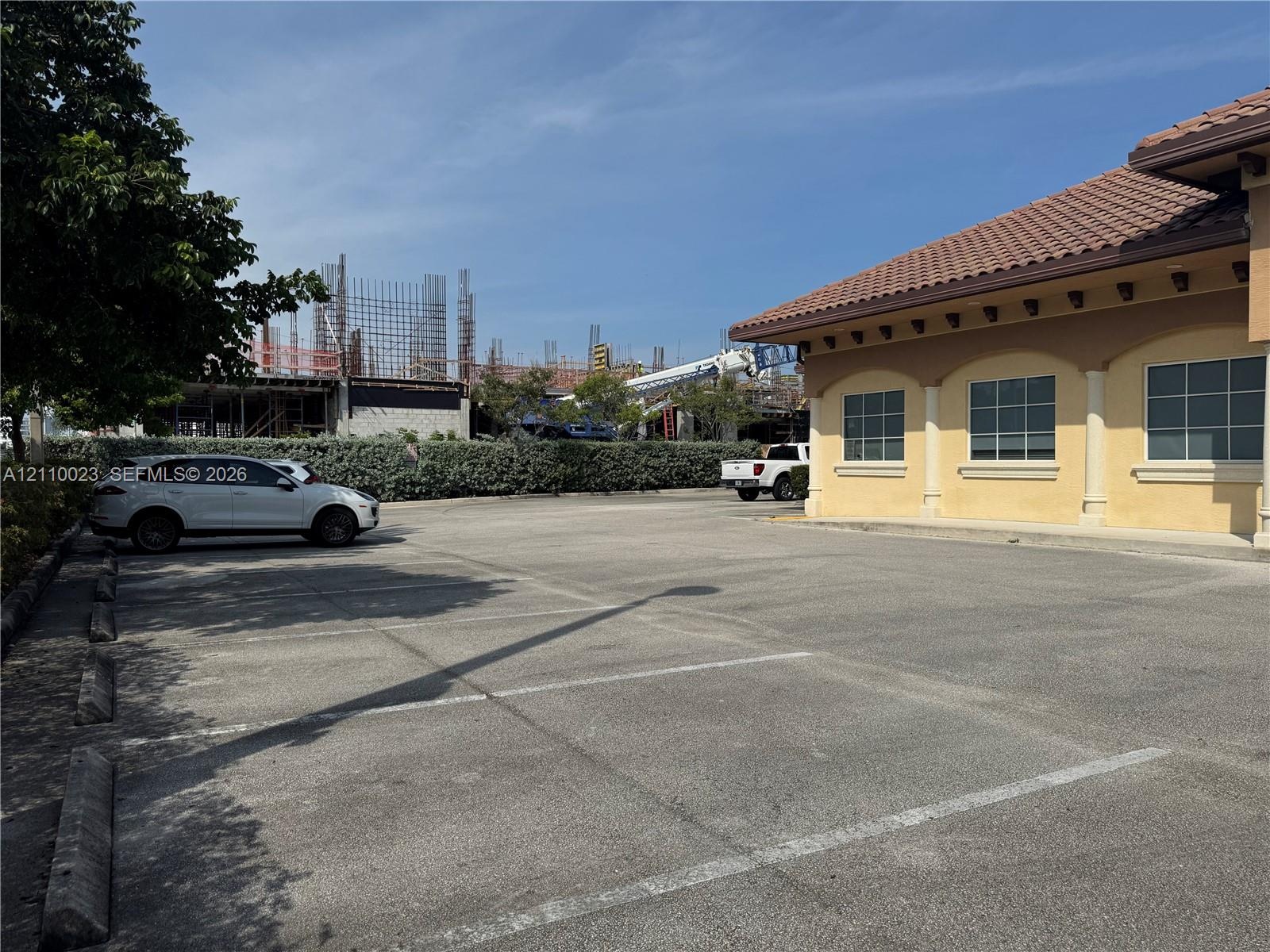 Paved parking area with concrete wheel stops, stucco exterior, clay tile roofing, and arched window frames