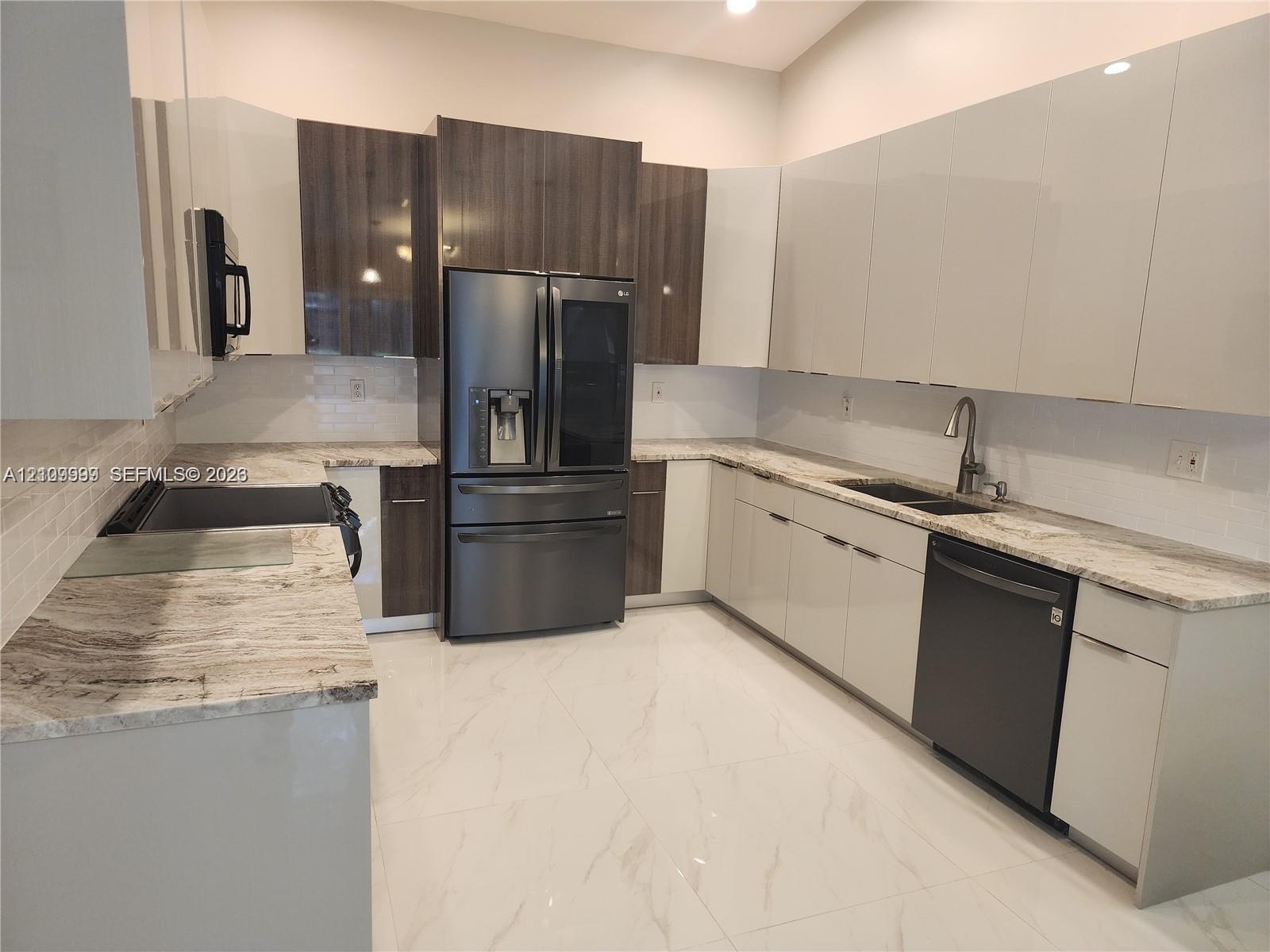 Kitchen featuring two-tone cabinetry with high-gloss finishes, stone countertops, large-format tile flooring, a double-basin undermount sink, and stai