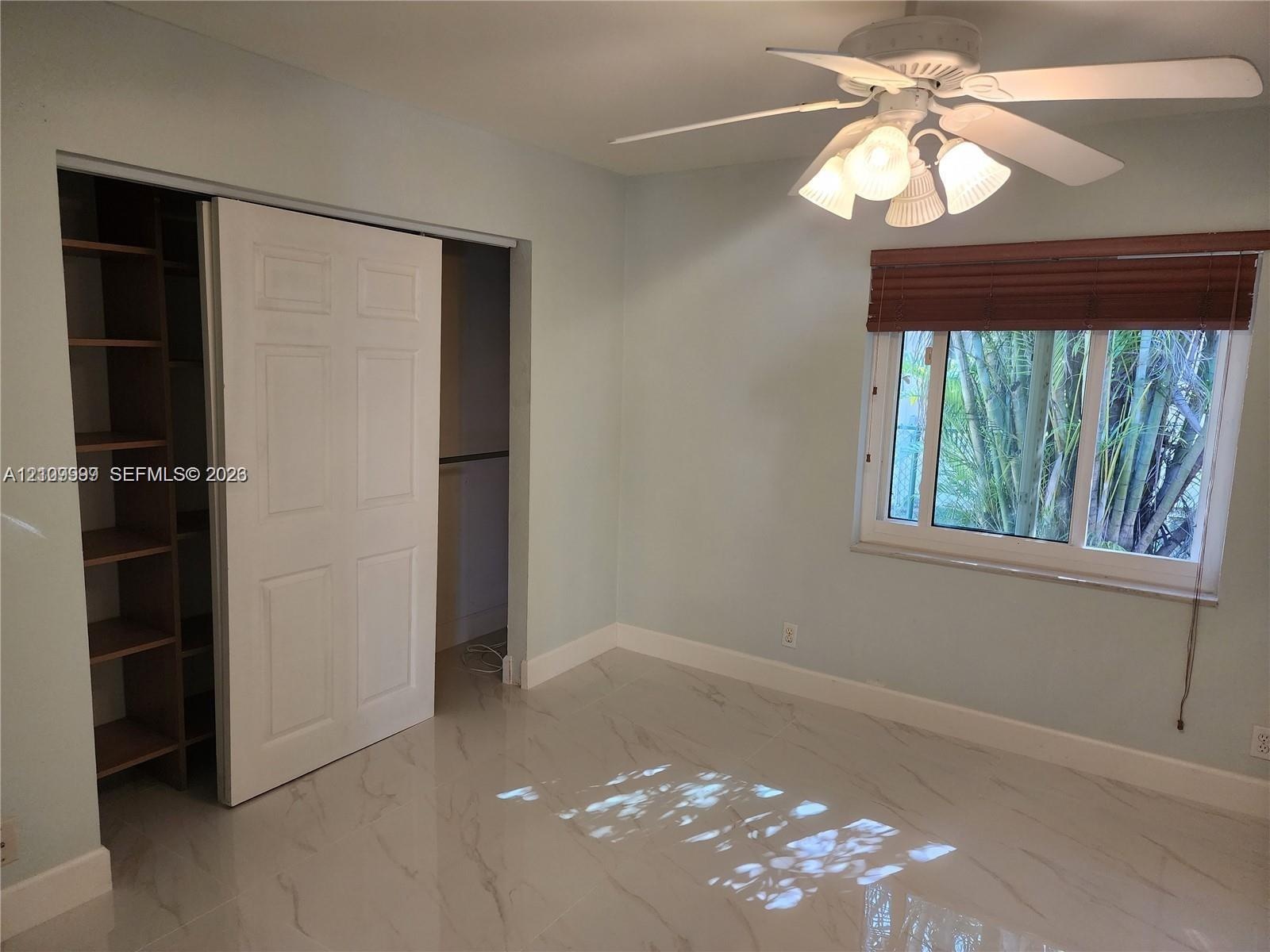 Large-format tile flooring, ceiling fan with integrated lighting, window with fitted blinds, and built-in closet shelving