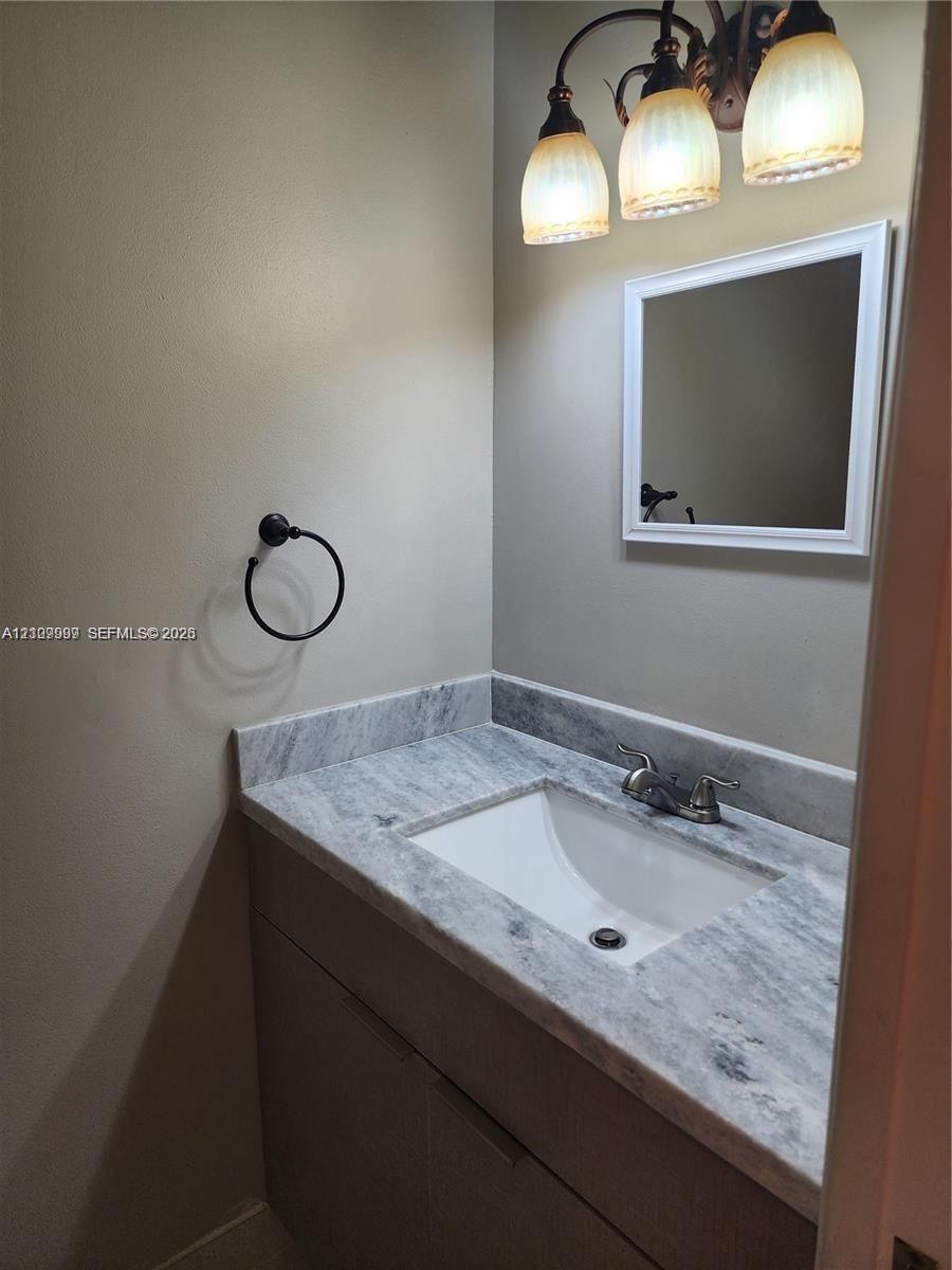 Vanity featuring a stone-surface countertop with an integrated rectangular sink, three-light decorative fixture, framed mirror, and matte black towel 