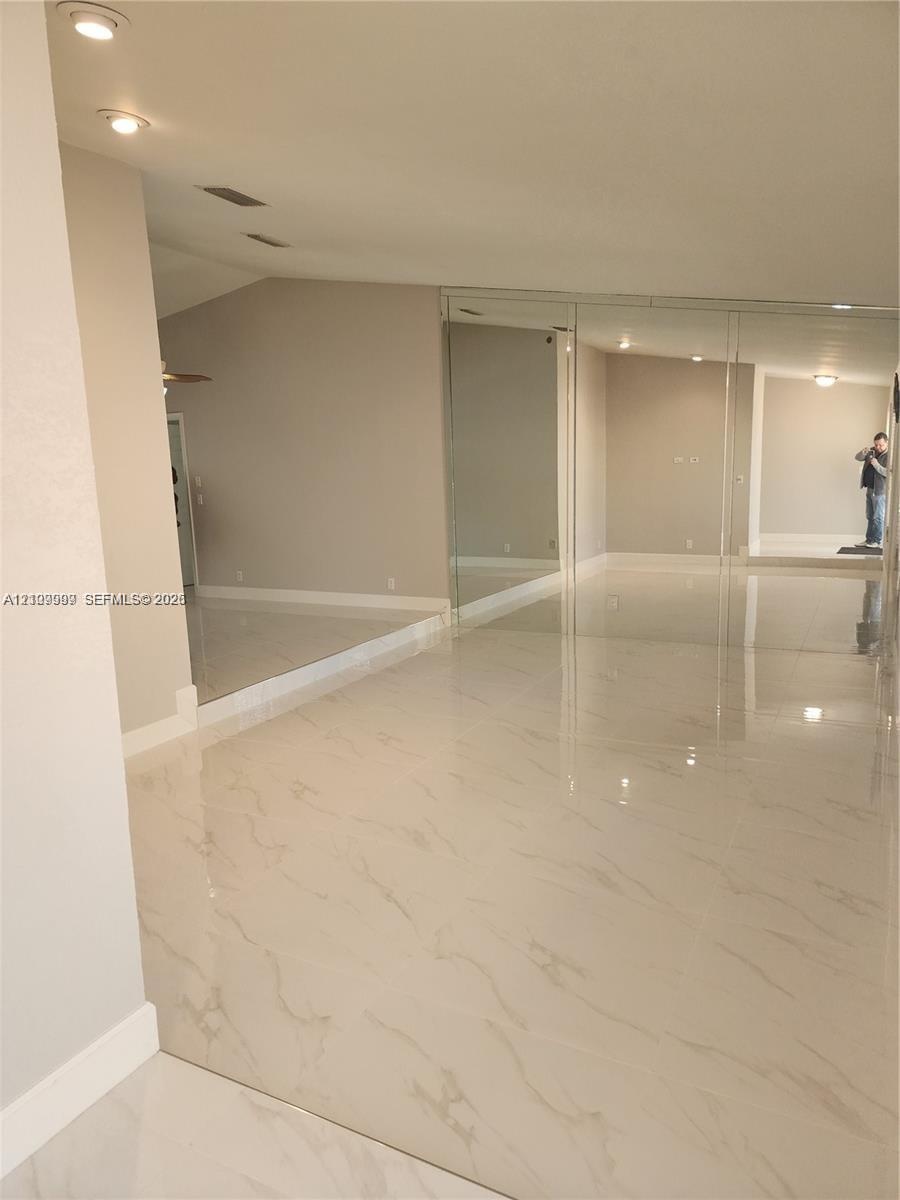 Polished stone-look tile flooring, vaulted ceilings, recessed lighting, and floor-to-ceiling mirrored closet doors