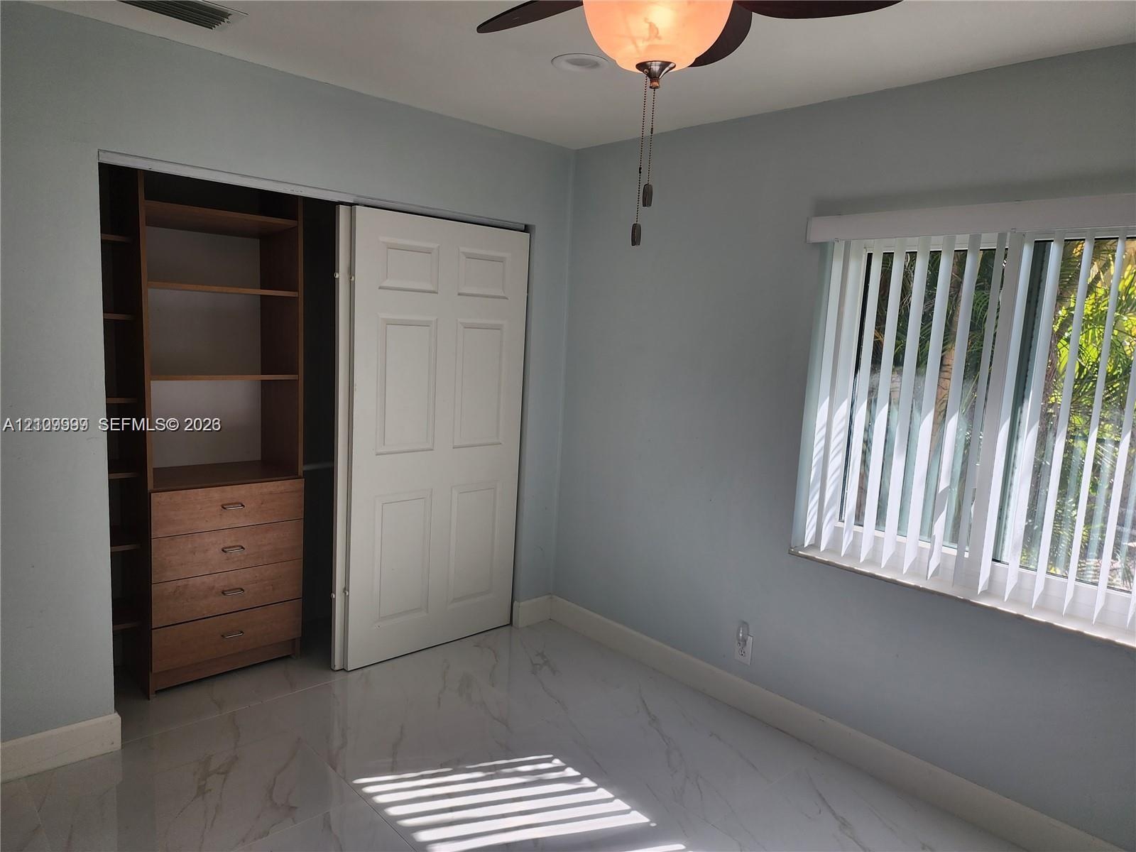Room featuring large-format tile flooring, a custom-built wood closet system with integrated shelving and drawers, a ceiling fan with integrated light