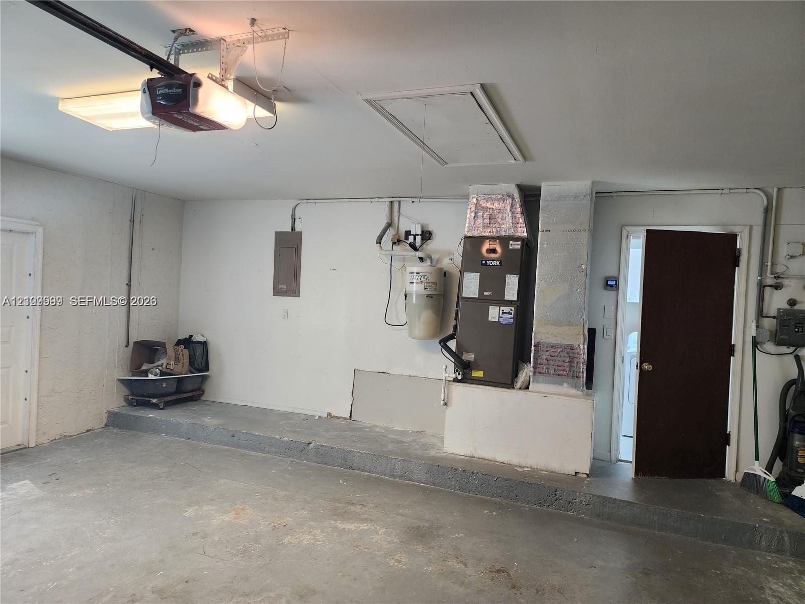 Garage featuring concrete flooring, an overhead automatic door opener, a dedicated HVAC unit, an electrical panel, and an access door