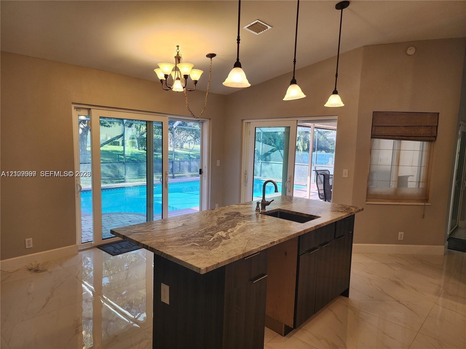Kitchen featuring an island with a stone countertop, dark wood-finish cabinetry, an undermount sink, a gooseneck faucet, and three pendant light fixtu