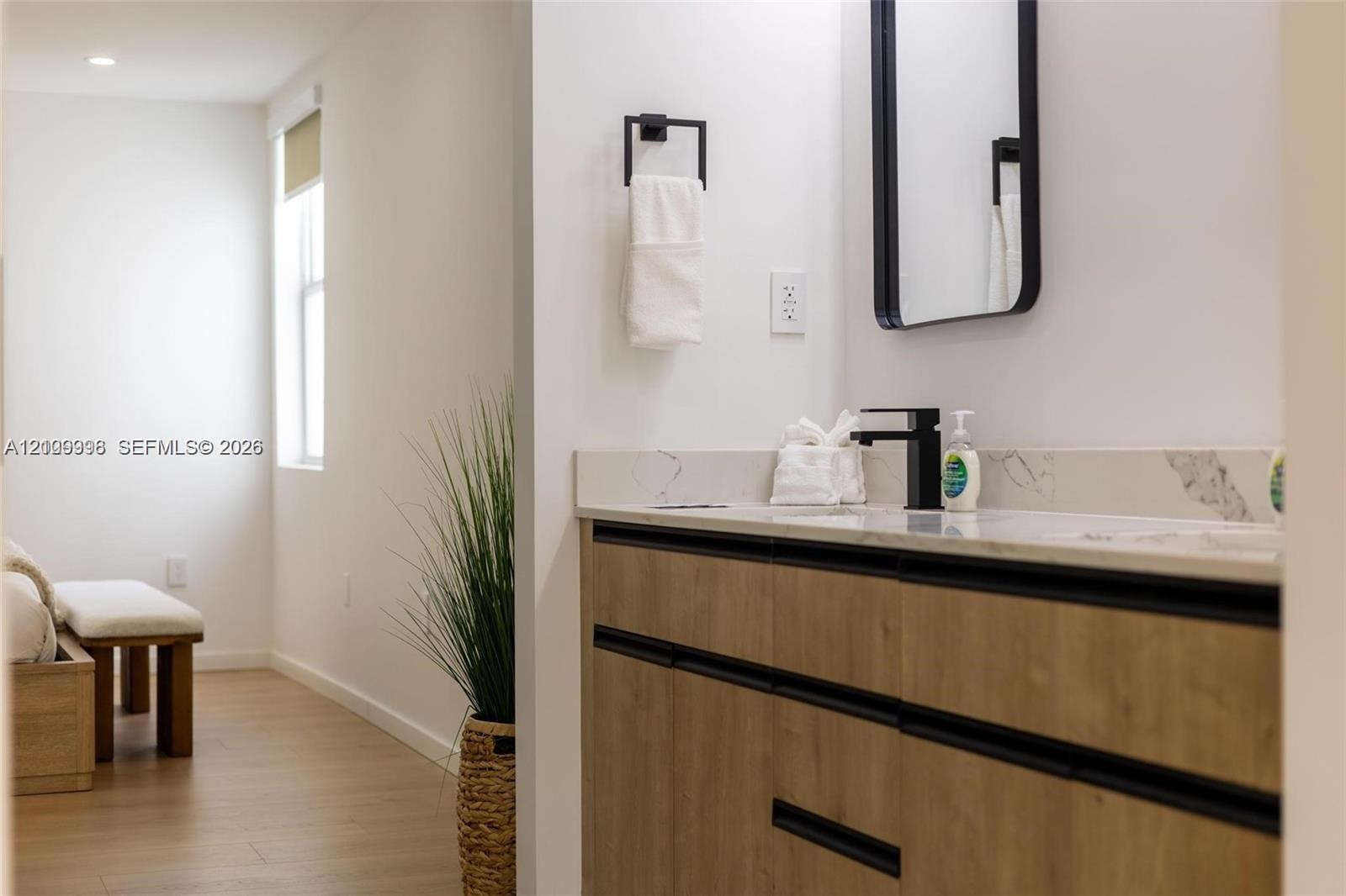 Floating vanity with wood-finish cabinetry, stone countertop, matte black faucet, and rectangular mirror with black frame