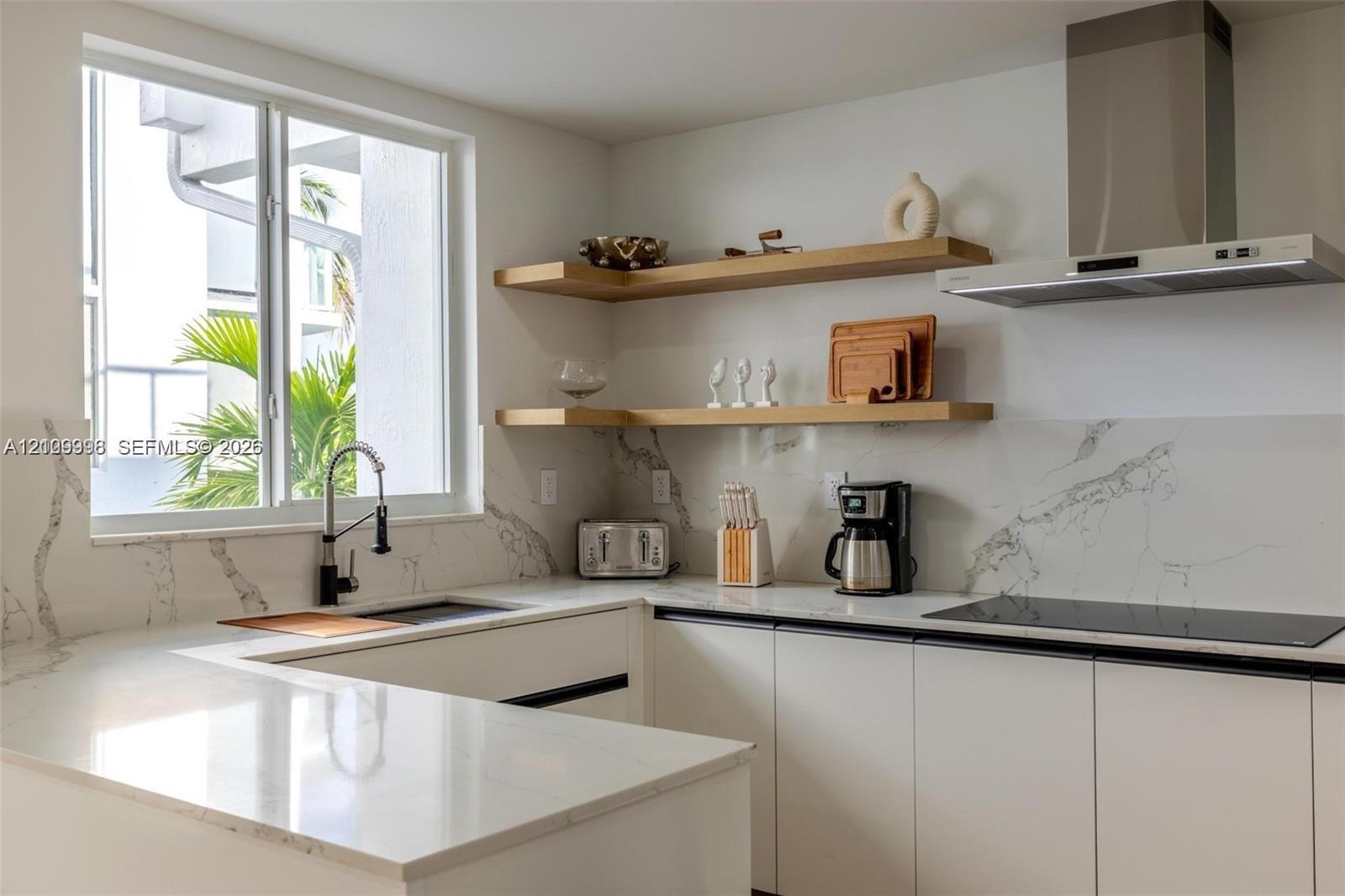 Kitchen featuring solid-surface countertops with matching full-height backsplash, flat-panel cabinetry, floating wood shelving, stainless steel range 
