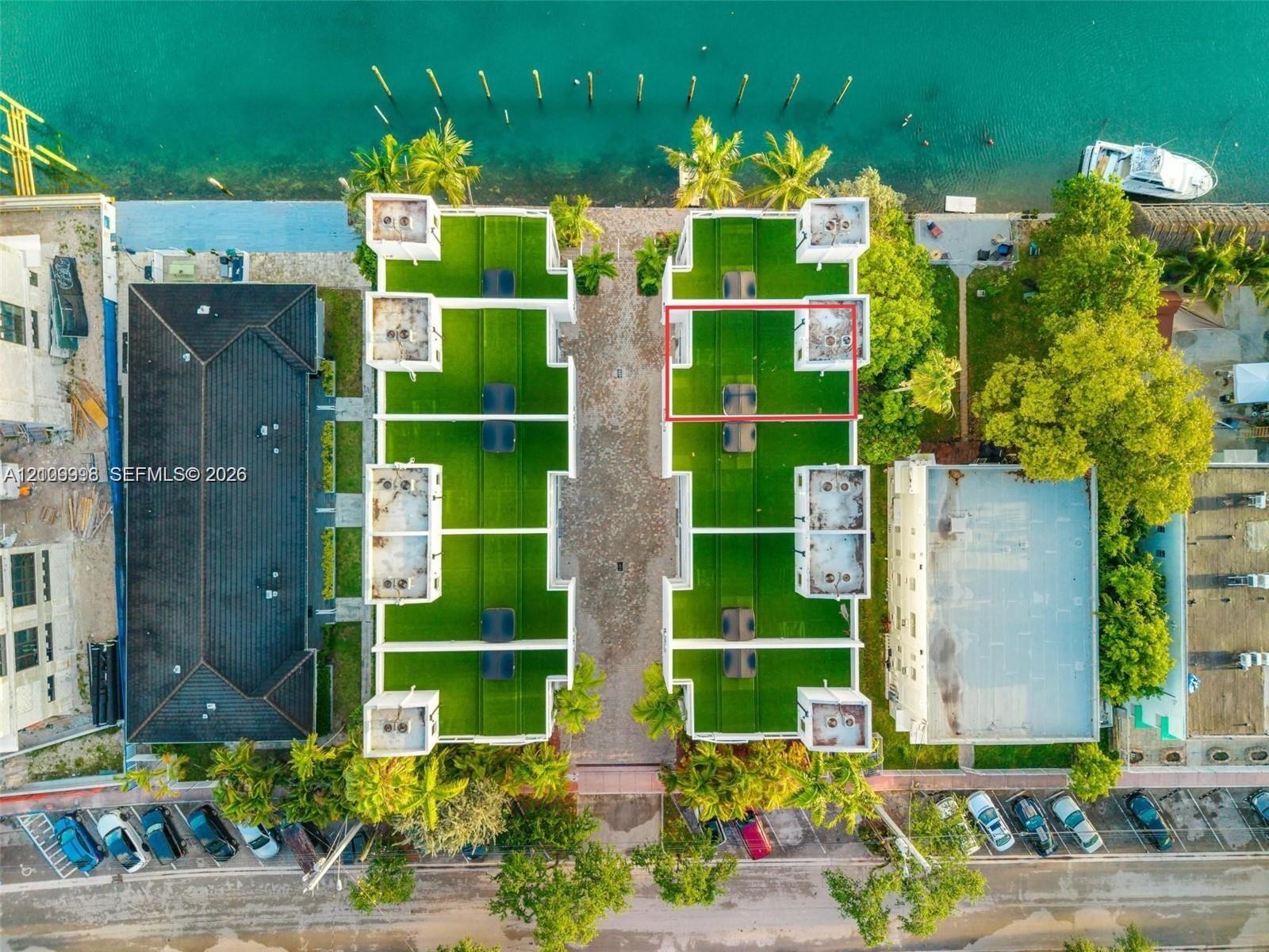 Aerial perspective featuring direct waterfront access, paved central driveway, rooftop artificial turf terraces, and established tropical vegetation