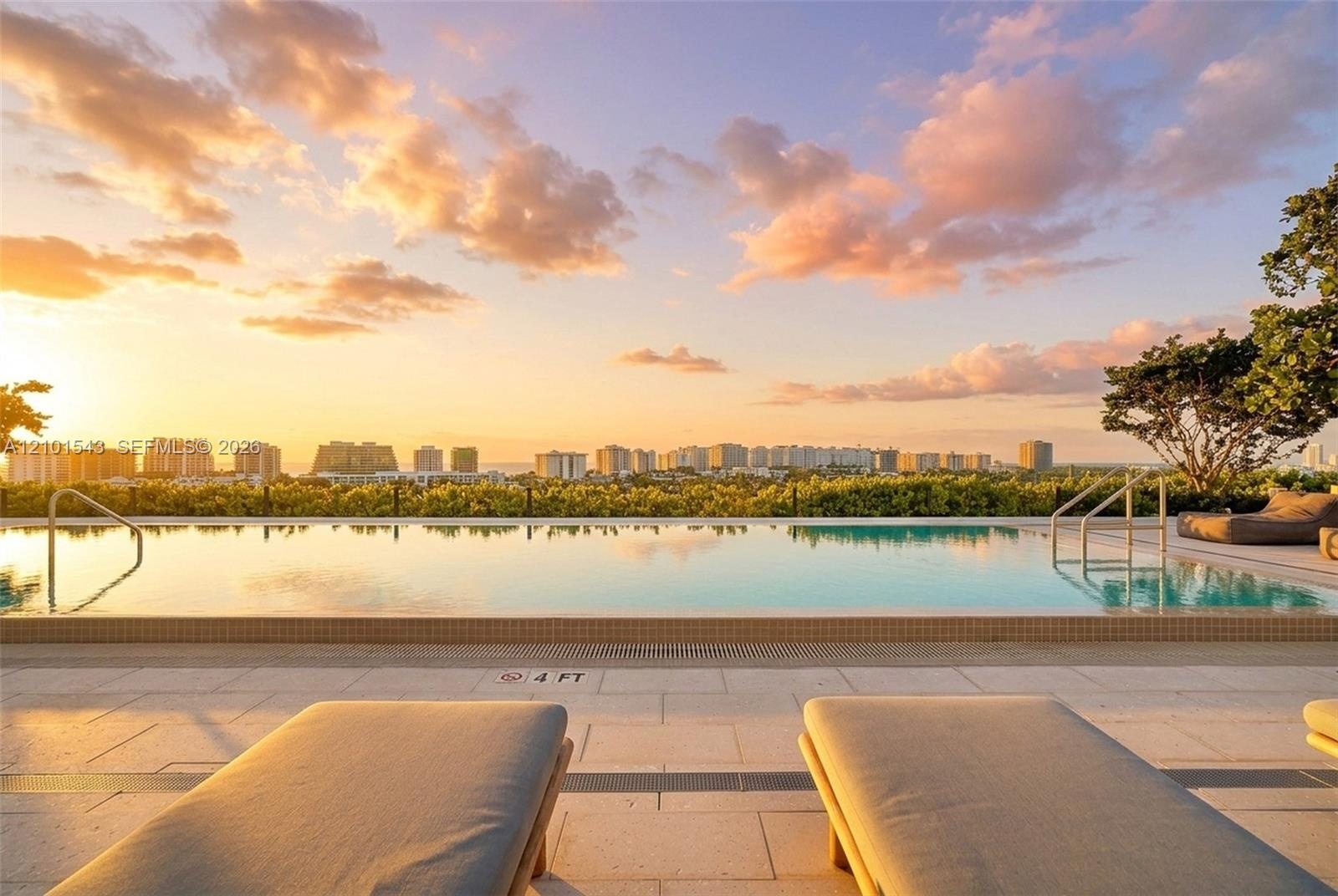 Infinity-edge swimming pool featuring stone tile decking, metal entry handrails, and a horizon backdrop