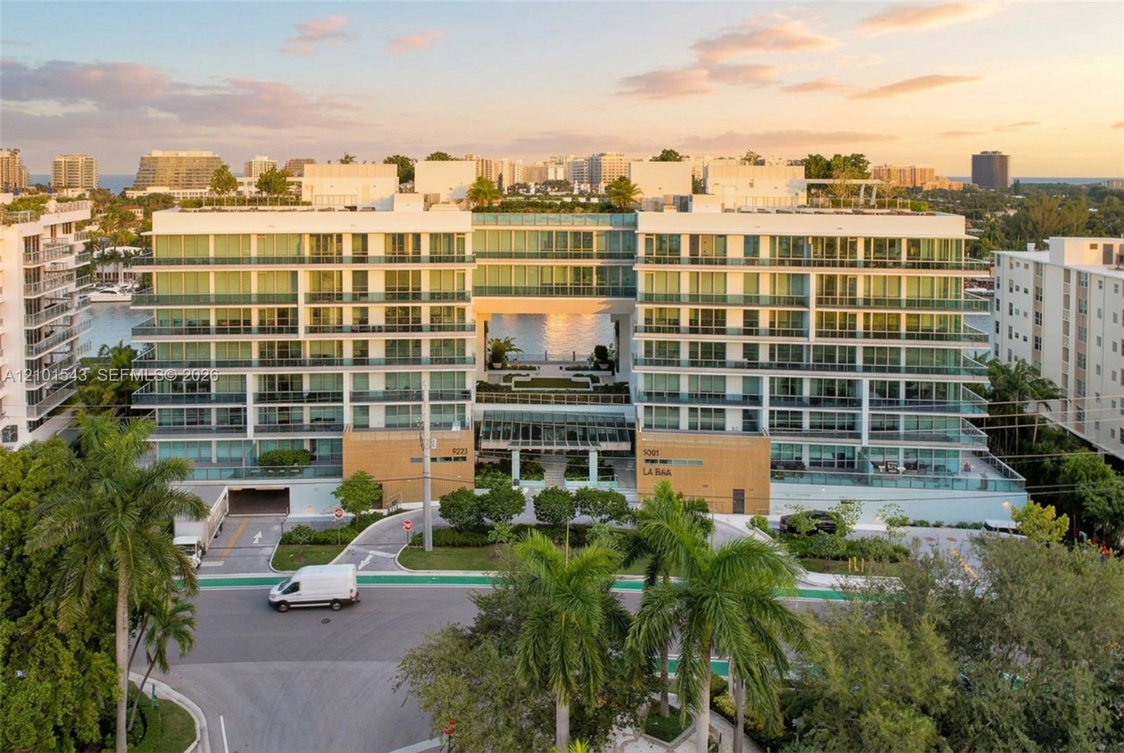 Mid-rise residential building featuring floor-to-ceiling glass paneling, wrap-around private balconies, and a central open-air atrium with ground-leve