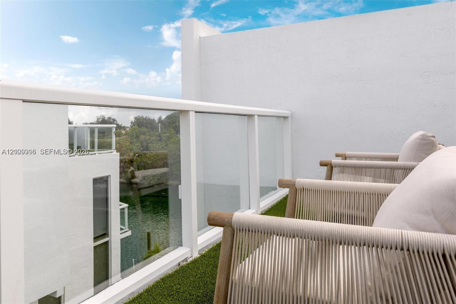 Private balcony featuring glass panel railing, white exterior stucco walls, and artificial turf flooring