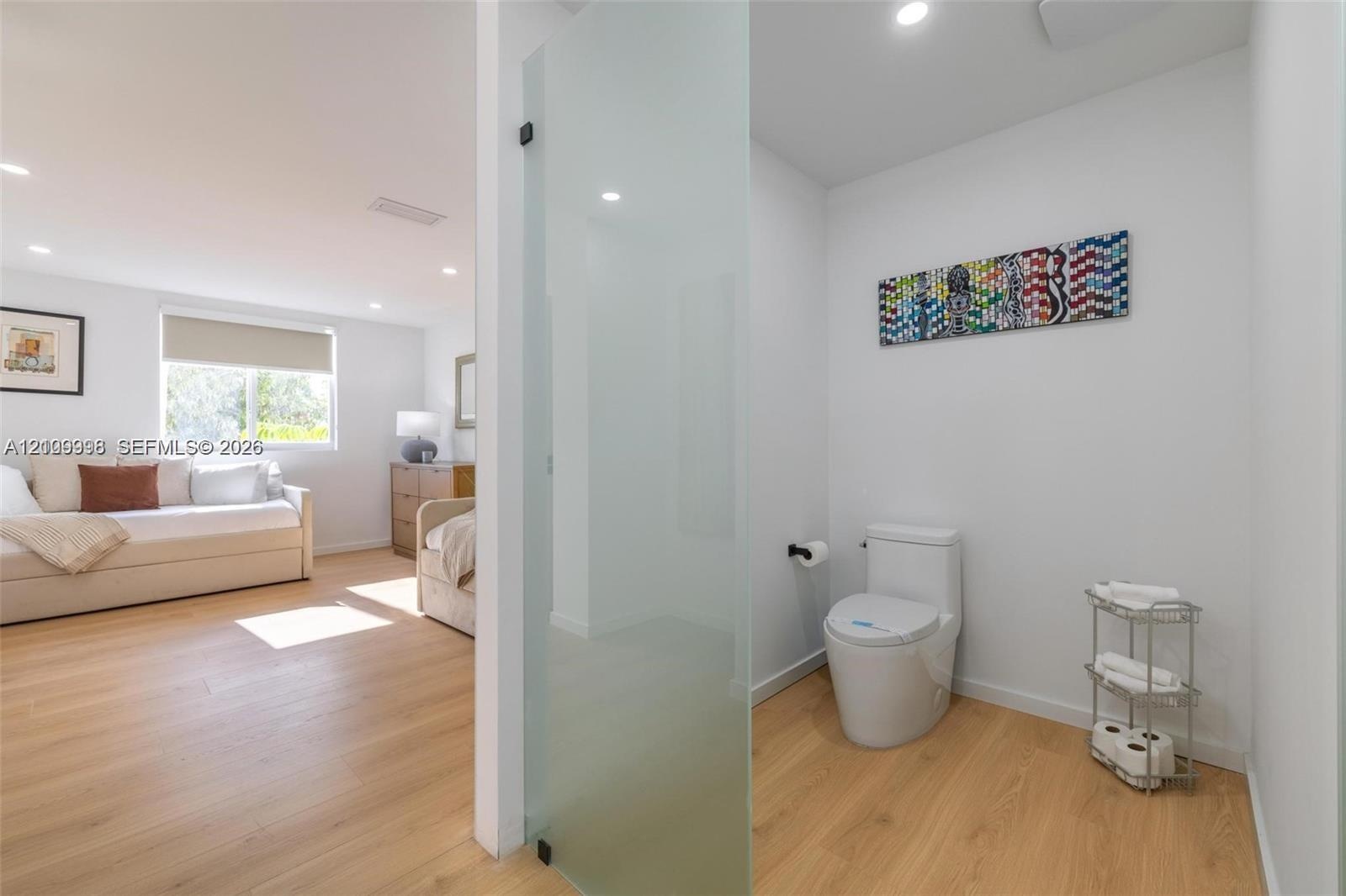 Wood-finish flooring, frosted glass enclosure, and modern one-piece toilet