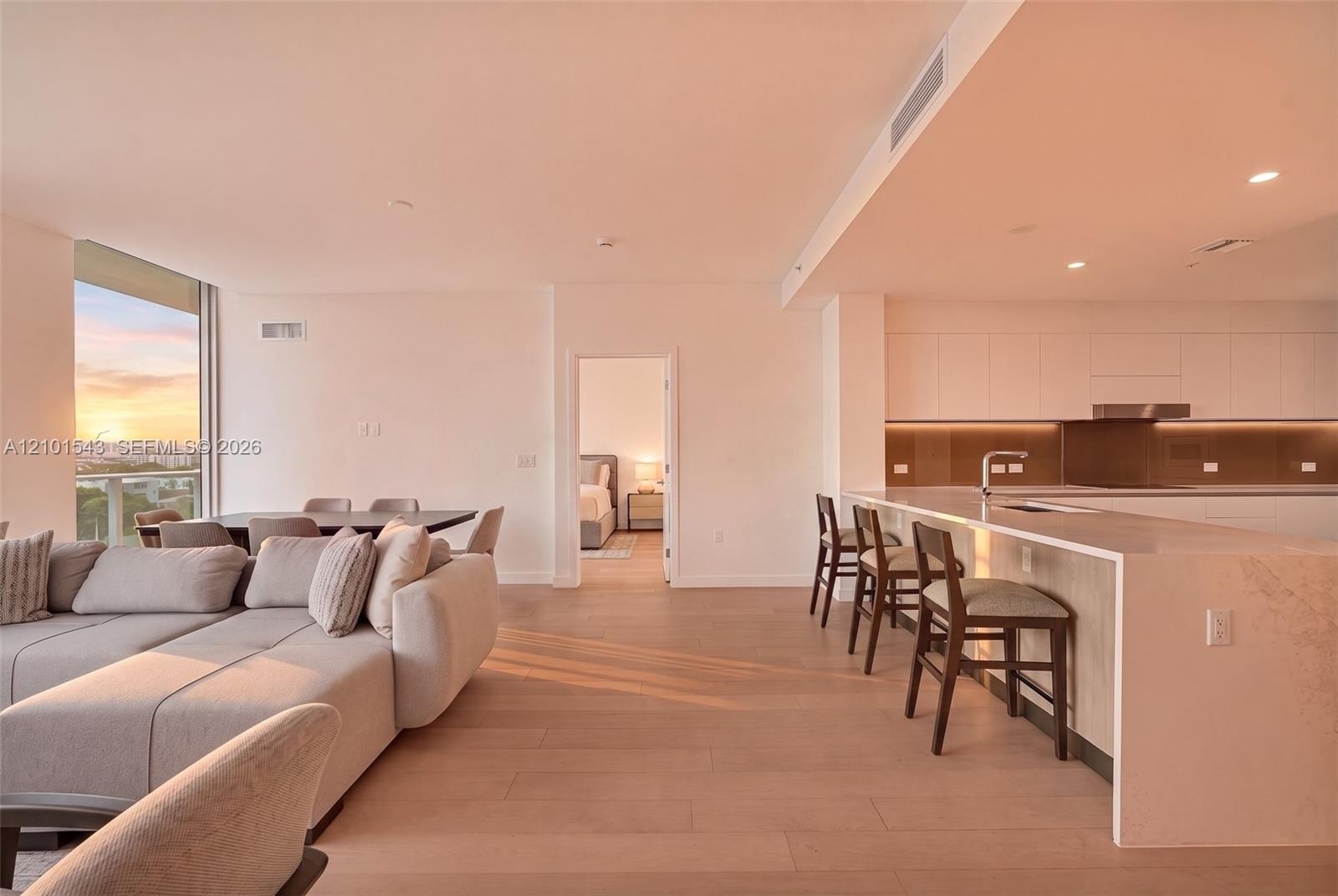 Open-concept interior featuring light wood-finish flooring, a kitchen with flat-panel cabinetry, a waterfall-edge countertop island, and recessed ceil
