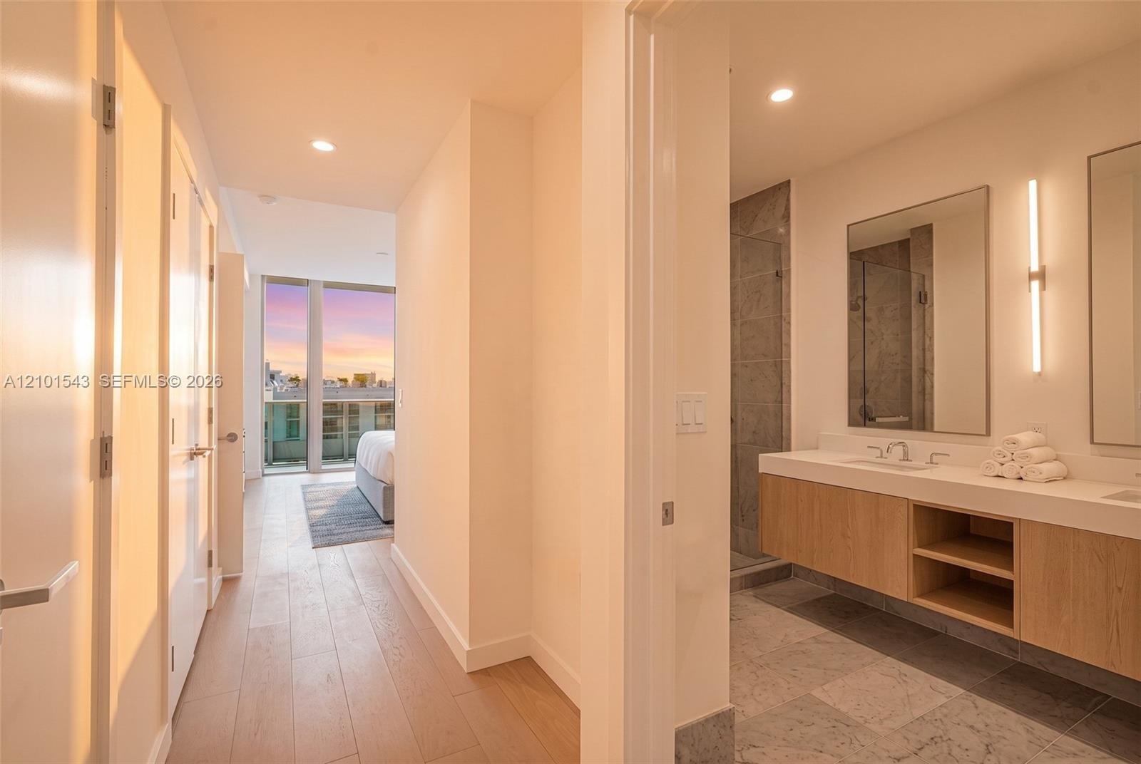 Floating wood-finish vanity with dual sinks, stone flooring, walk-in tile shower with glass enclosure, recessed lighting, and wall-mounted vanity mirr