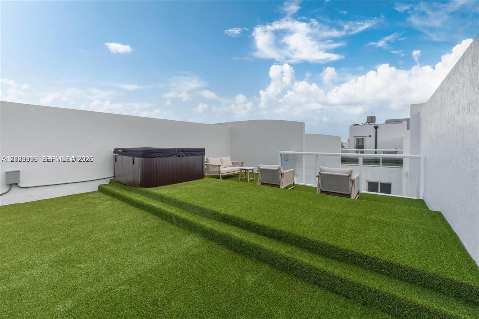 Rooftop terrace featuring tiered synthetic turf flooring, built-in hot tub, and glass perimeter railings