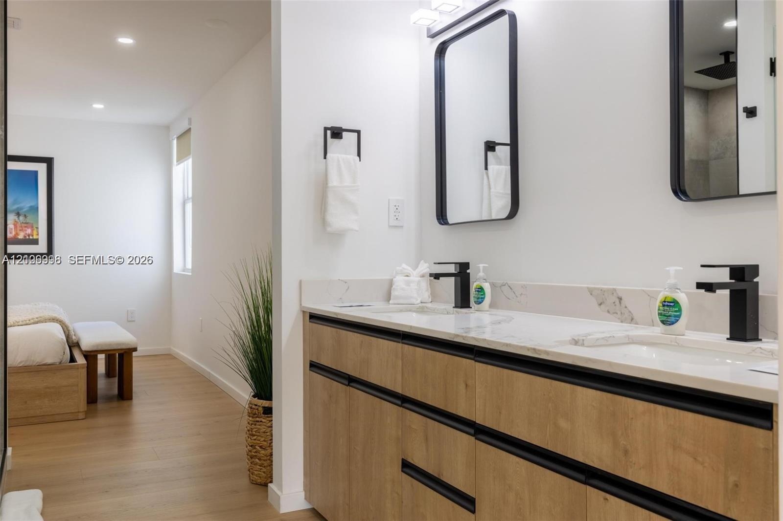 Modern vanity with wood-finish cabinetry, dual undermount sinks, stone-finish countertops, matte black fixtures, and rectangular mirrors