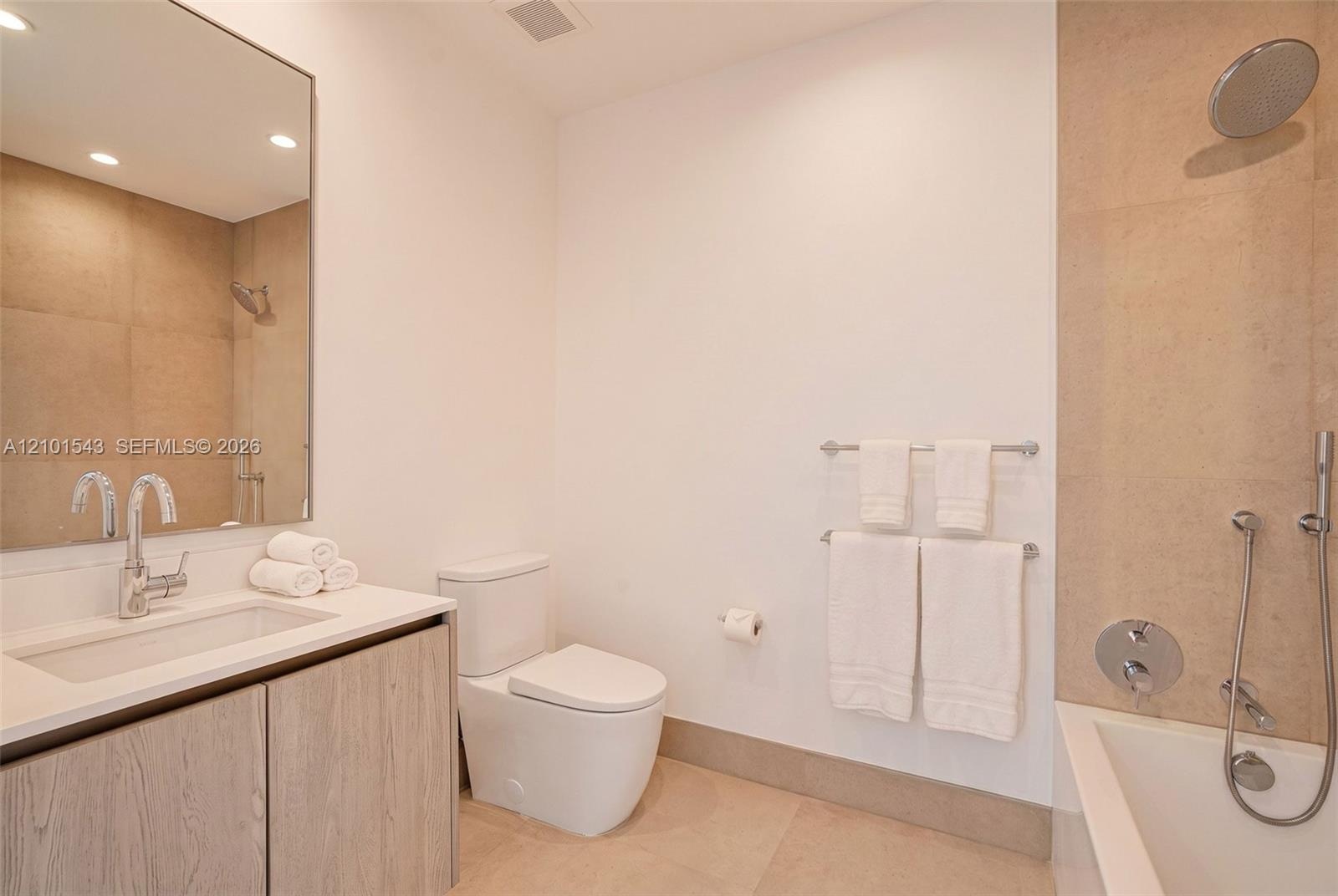 Bathroom featuring wood-finish cabinetry, a white rectangular sink, large-format tile surround, chrome wall-mounted fixtures, and a glass-enclosed soa