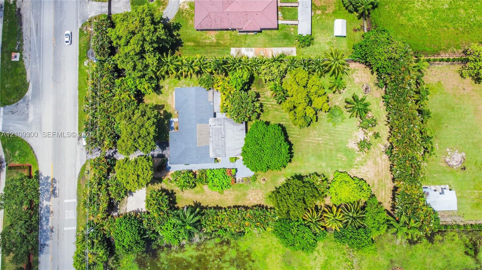Aerial view featuring a expansive lot, perimeter landscaping, mature trees, and a paved driveway