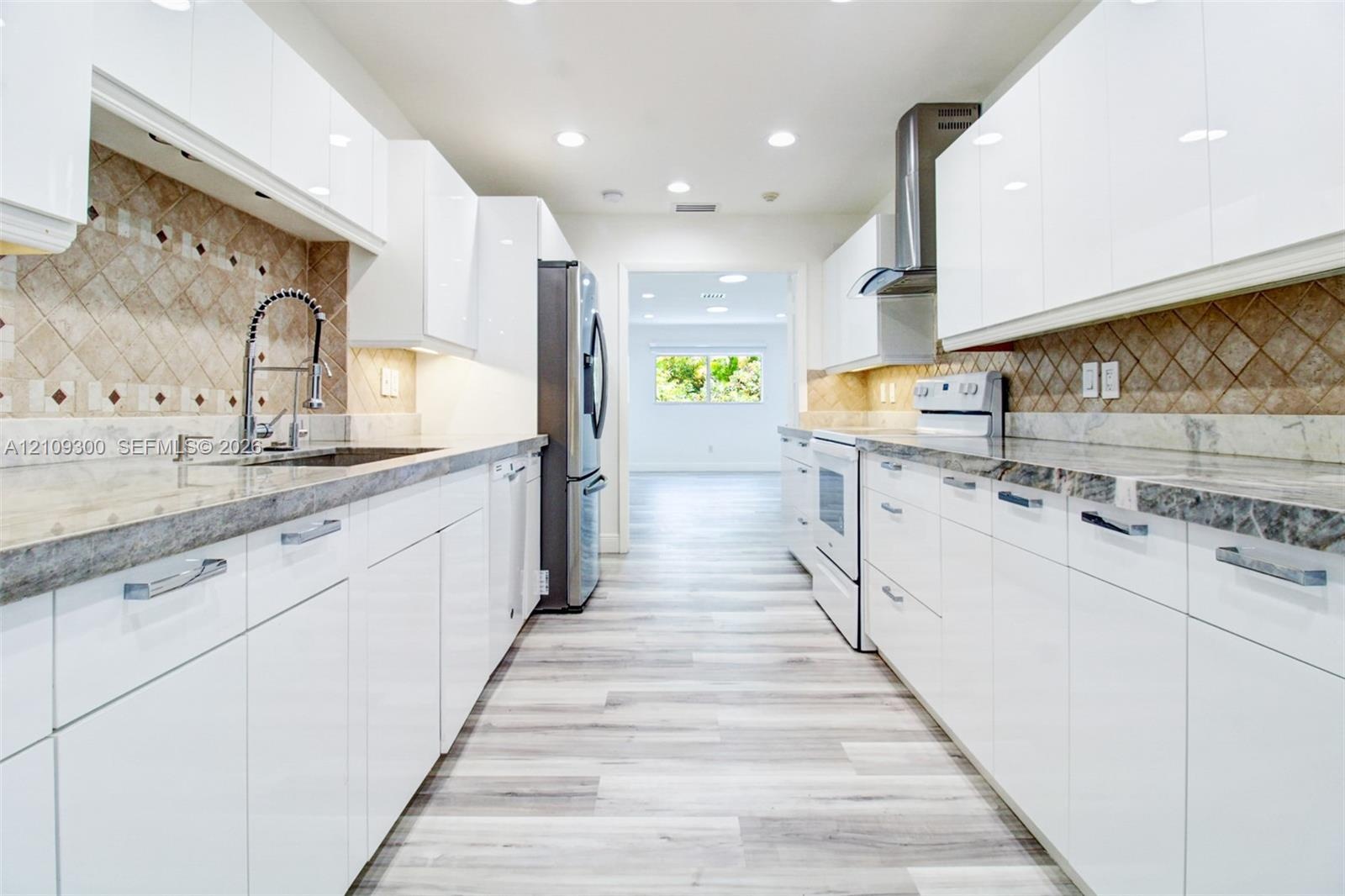 Kitchen featuring high-gloss white cabinetry, stone countertops, stainless steel appliances, a diagonal-patterned tile backsplash, and wood-finish flo