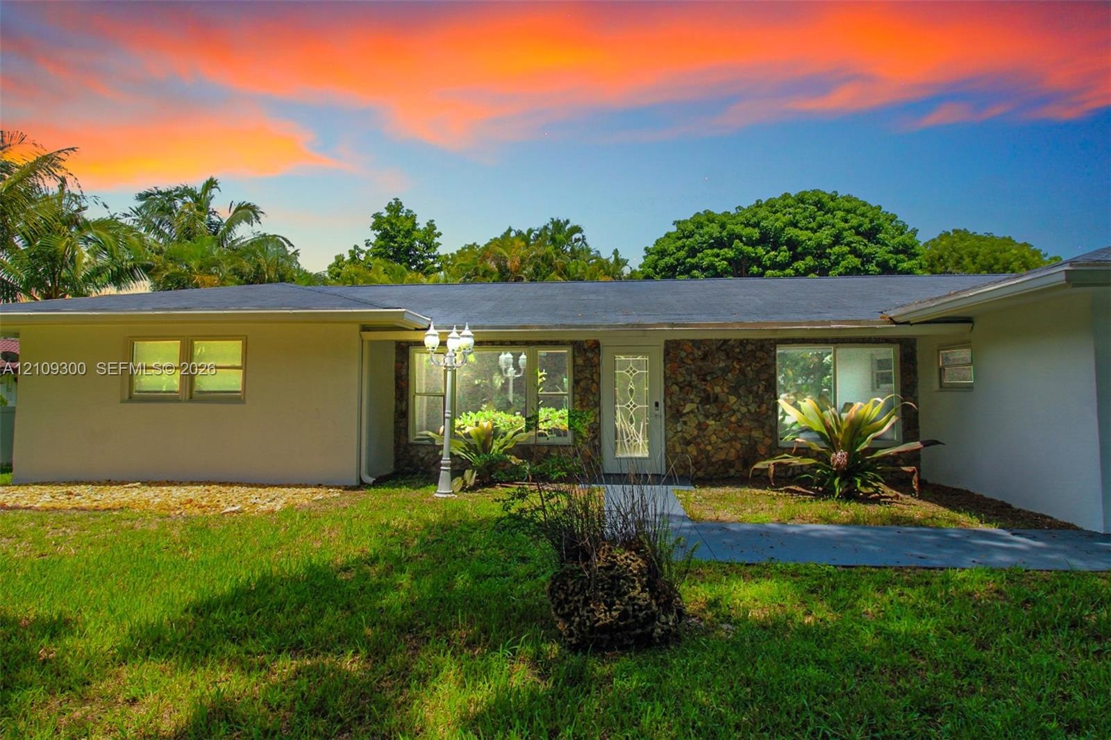 Single-story exterior featuring light-toned stucco, natural stone masonry accents, a decorative glass-panel front door, and a multi-paneled roof