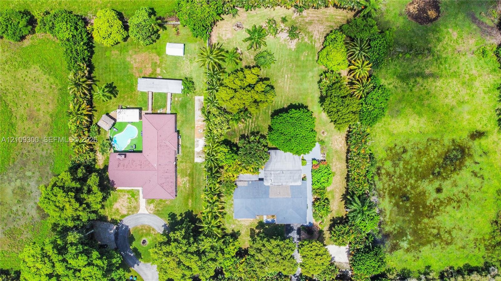 Aerial perspective of a sprawling property featuring two distinct residential structures, a swimming pool, mature perimeter landscaping, and expansive