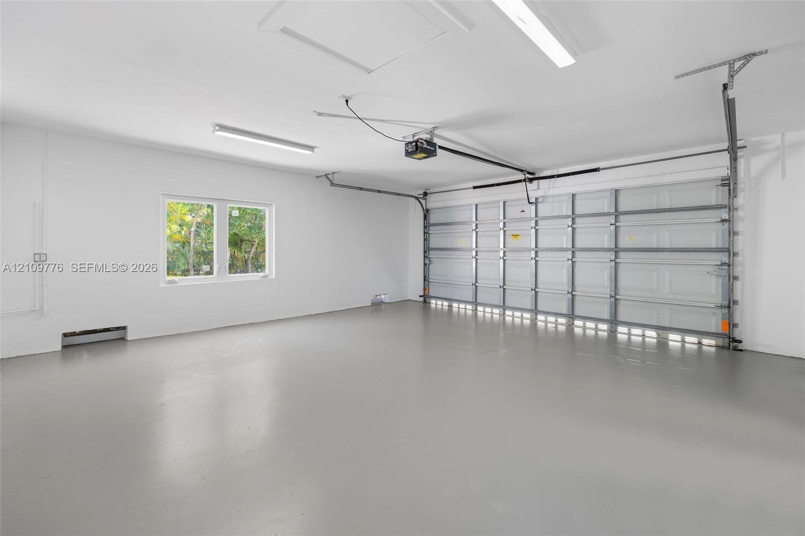 Multi-car garage featuring a smooth-finish floor, white walls, dual overhead fluorescent lighting, and an automatic sectional door