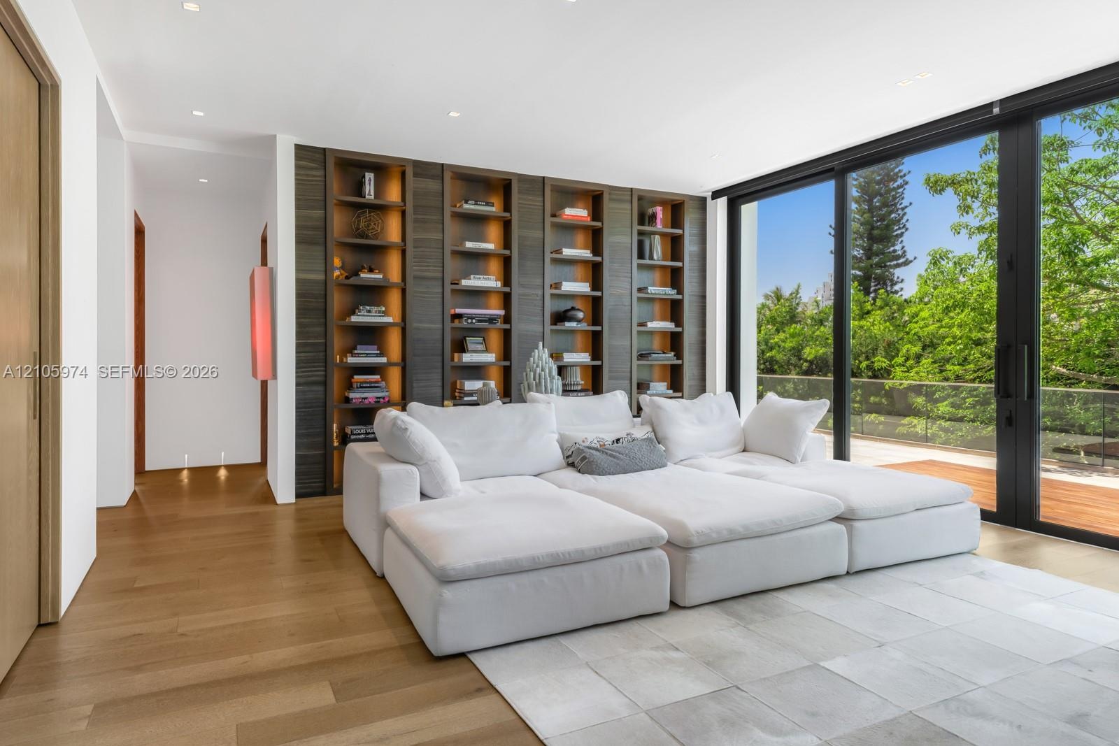 Custom floor-to-ceiling built-in shelving with integrated warm lighting, wide-plank wood-finish flooring, and expansive floor-to-ceiling sliding glass