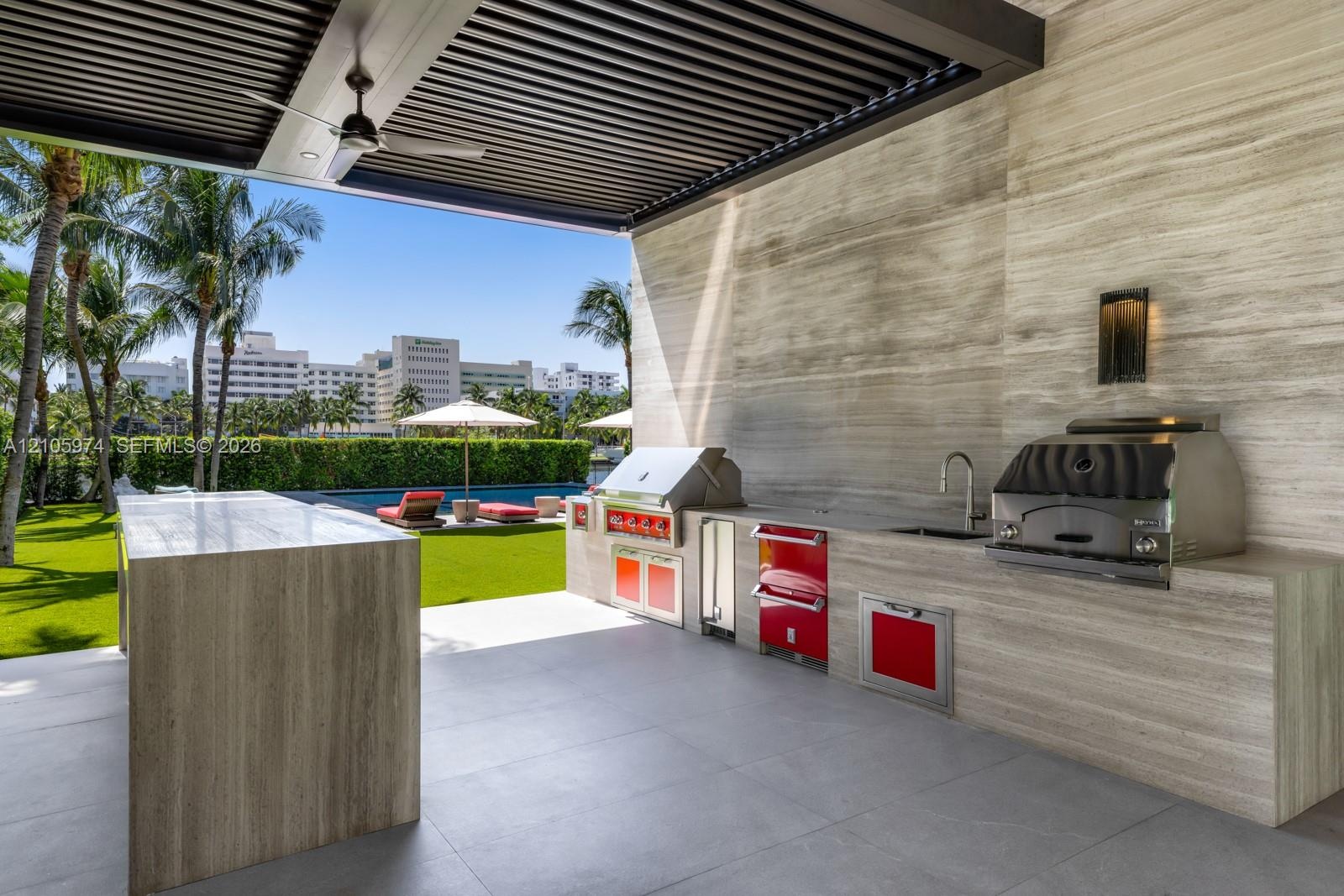 Covered outdoor kitchen featuring stone-clad surfaces, stainless steel built-in grill and beverage refrigeration, integrated faucet, and an overhead l